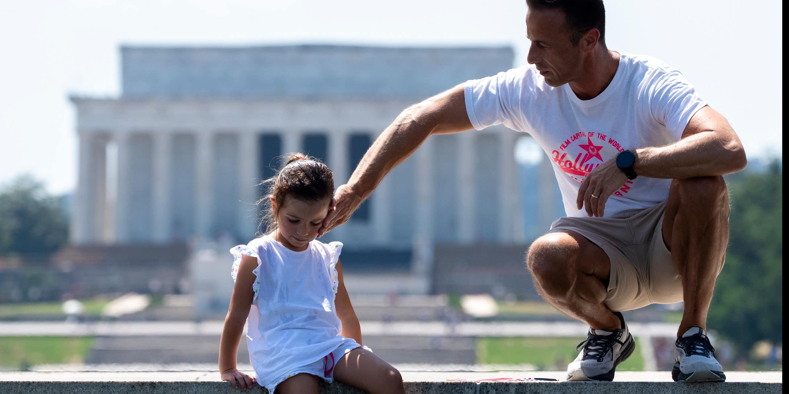 A man and a young girl are pictured in front of a monument.