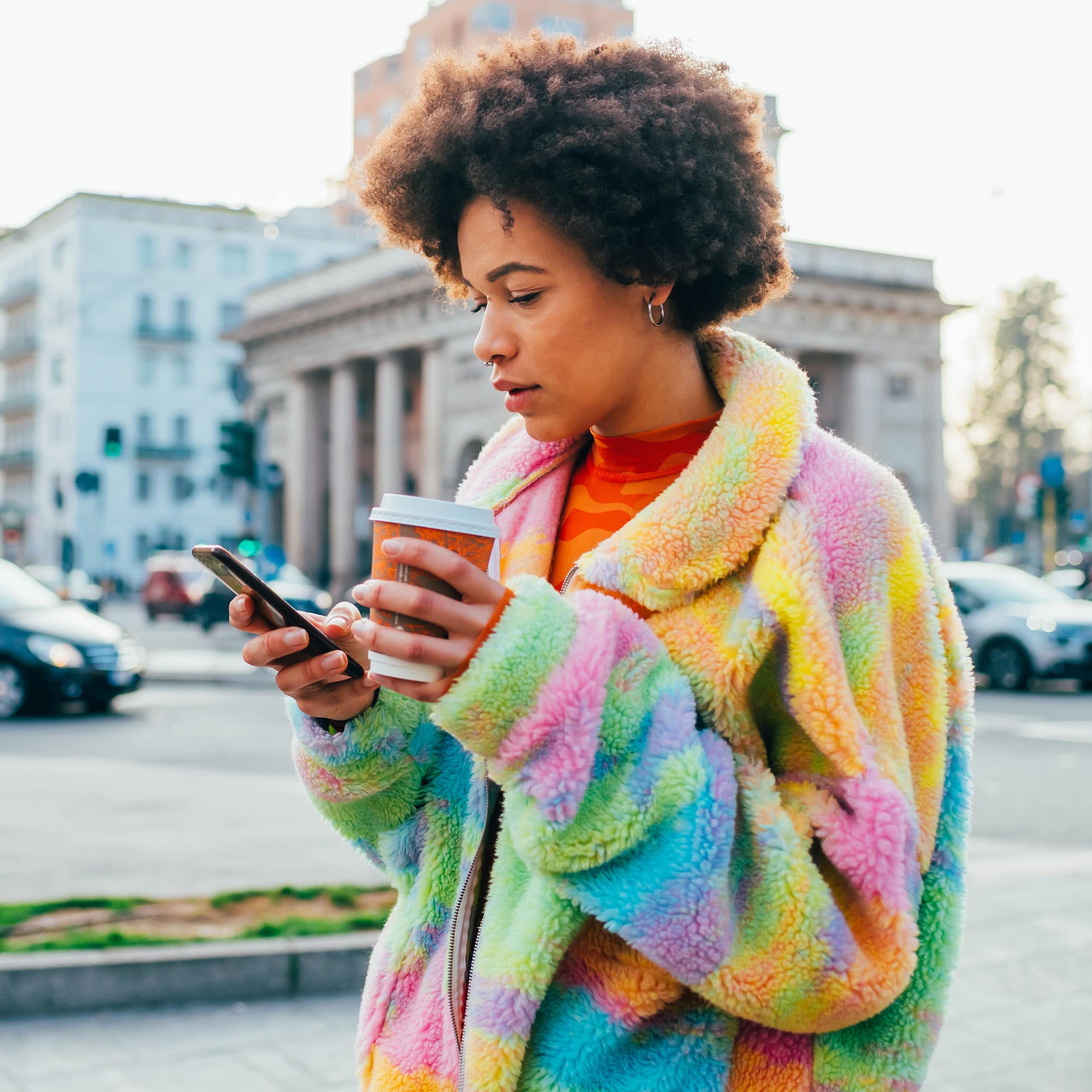 A young woman holding a reusable coffee cup while using a smartphone