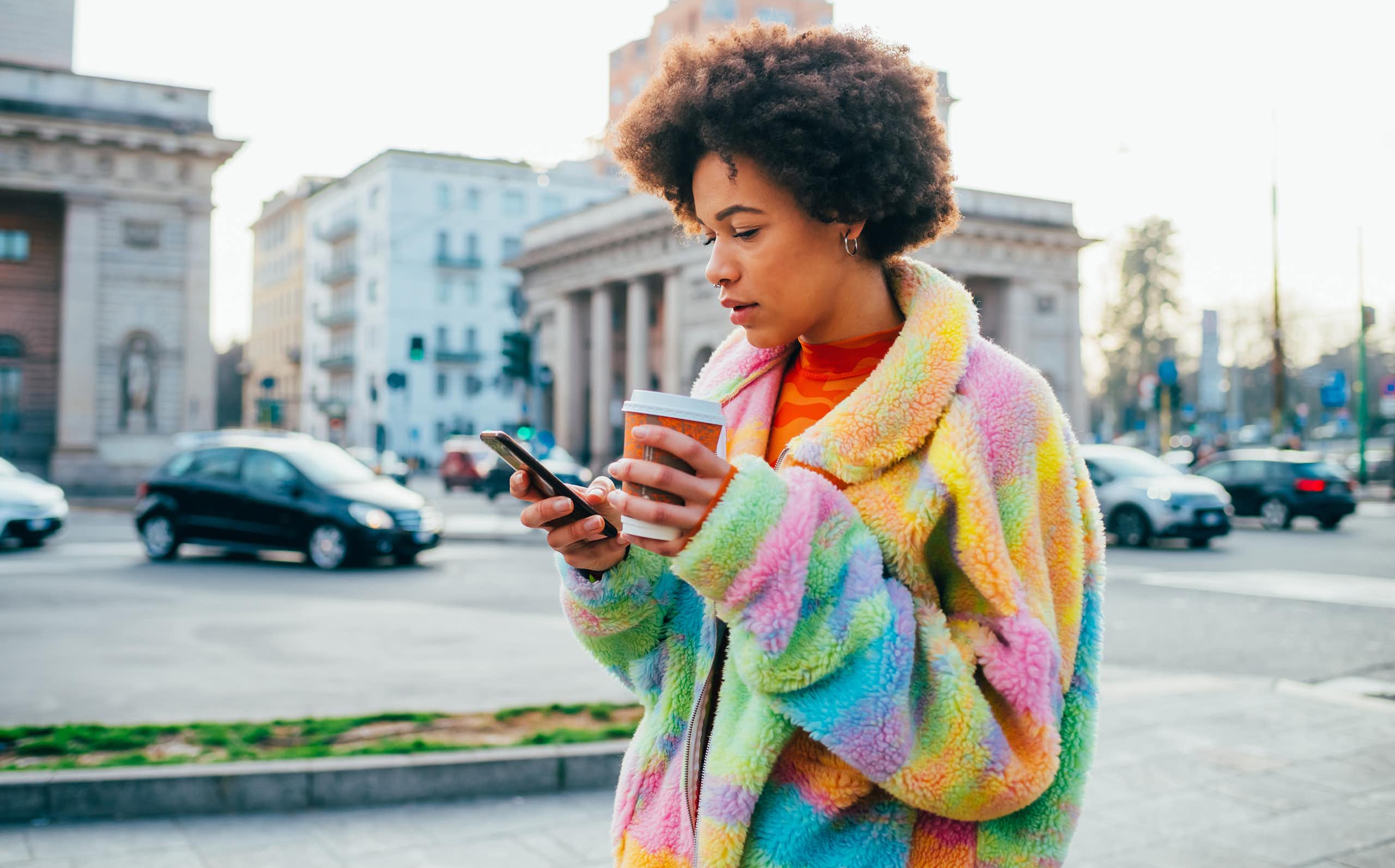 A young woman holding a reusable coffee cup while using a smartphone