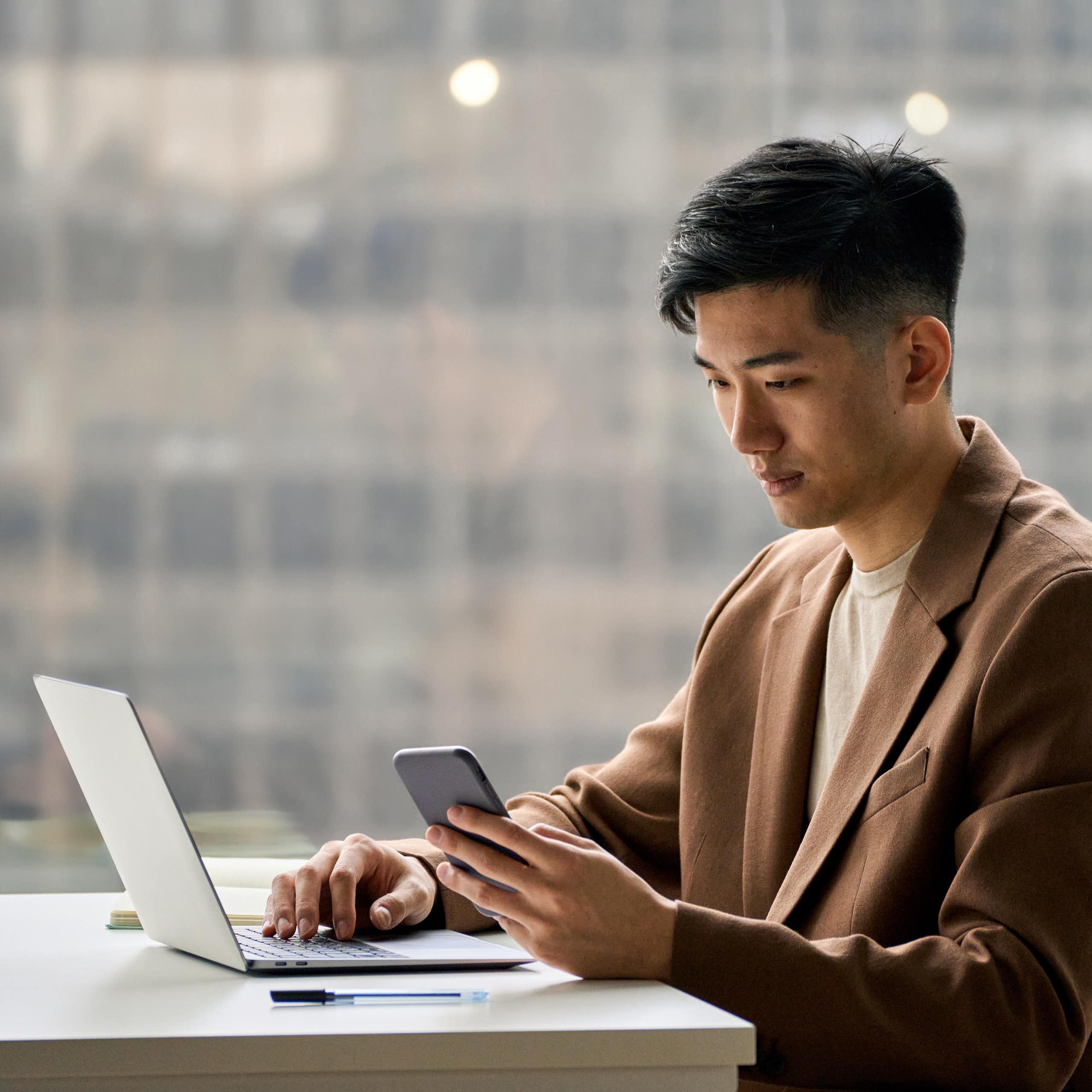 A man sits at a desk looking at his phone.