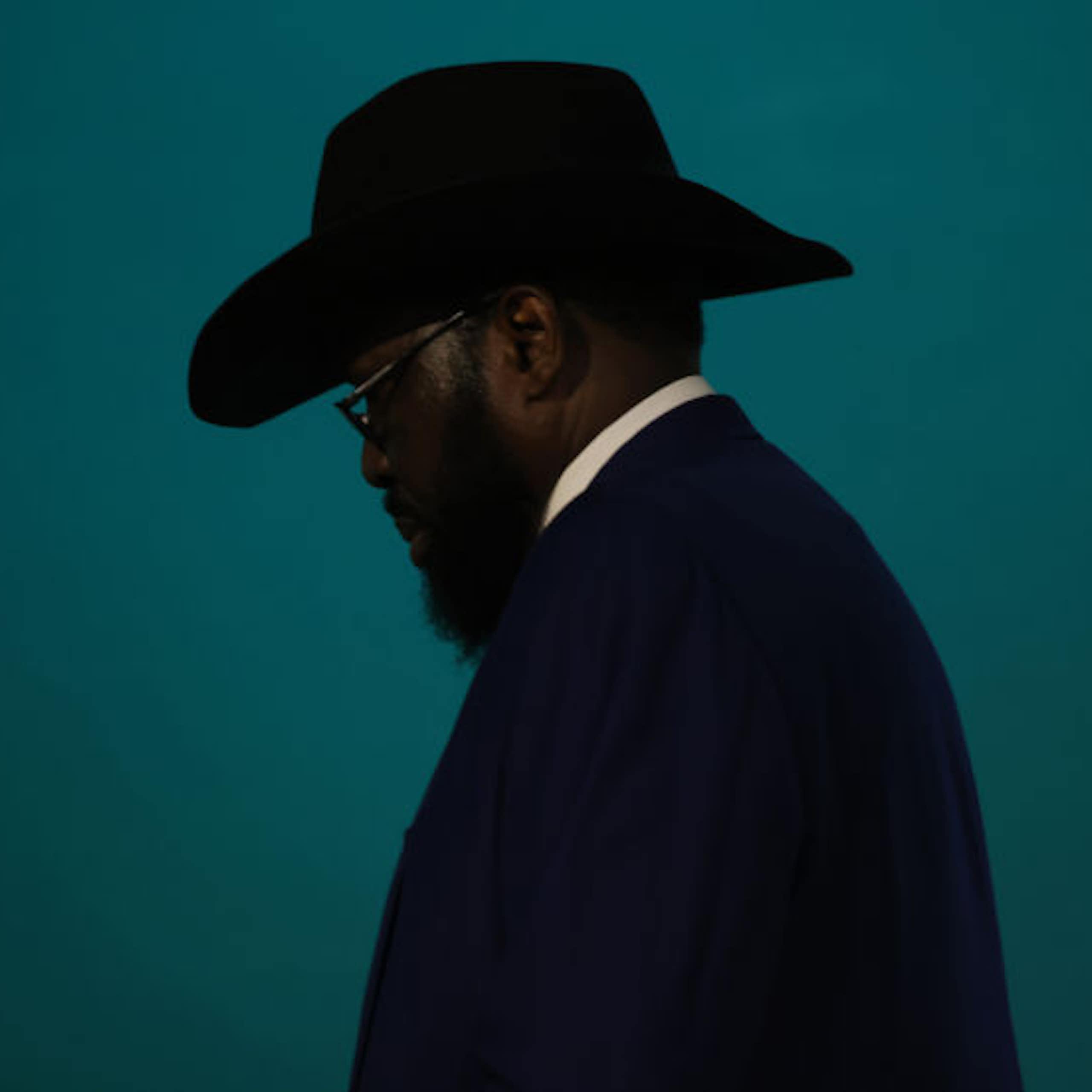 Profile of a man wearing a dark hat, with spectacles and a beard