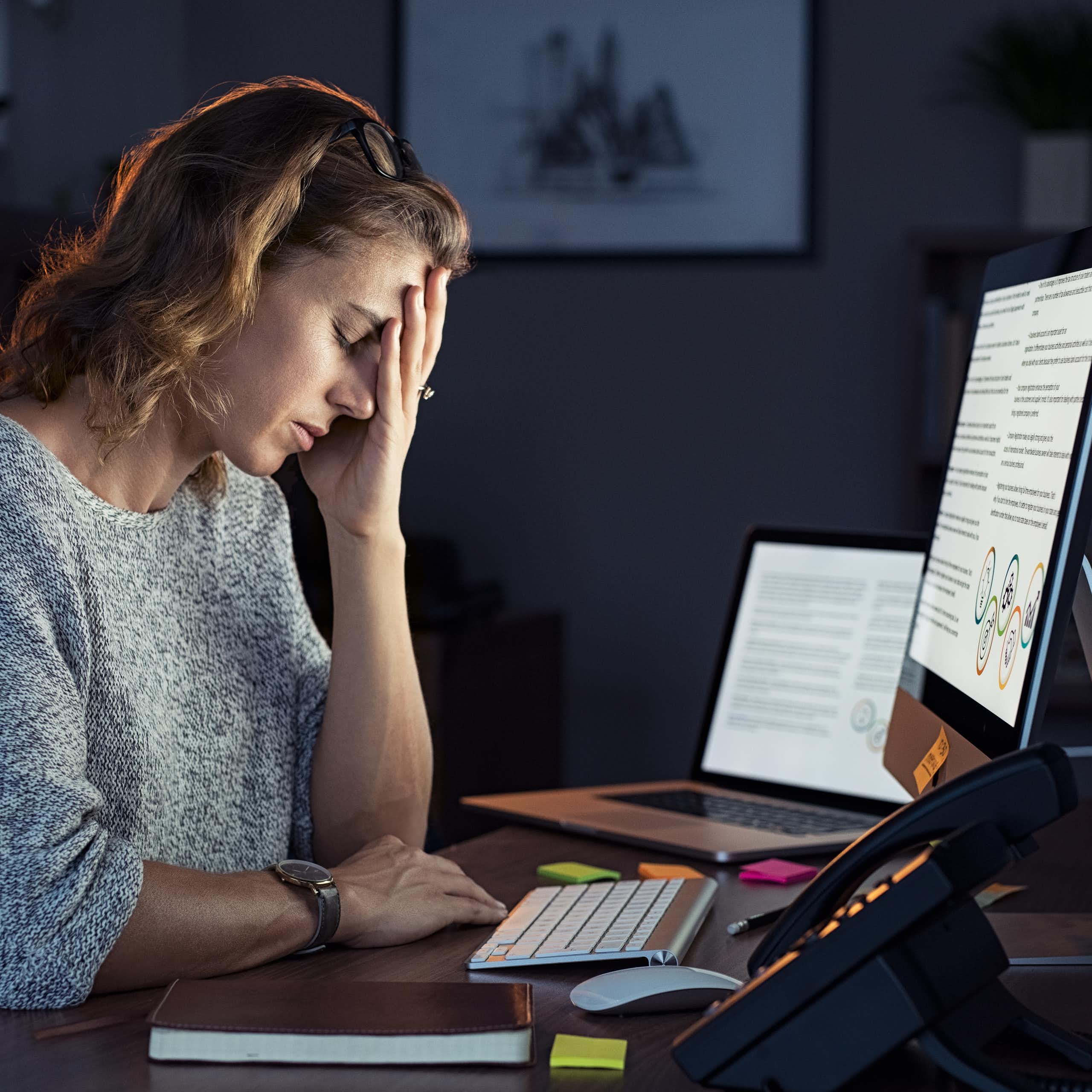 Une femme assise devant un ordinateur à un bureau repose sa tête sur sa main.