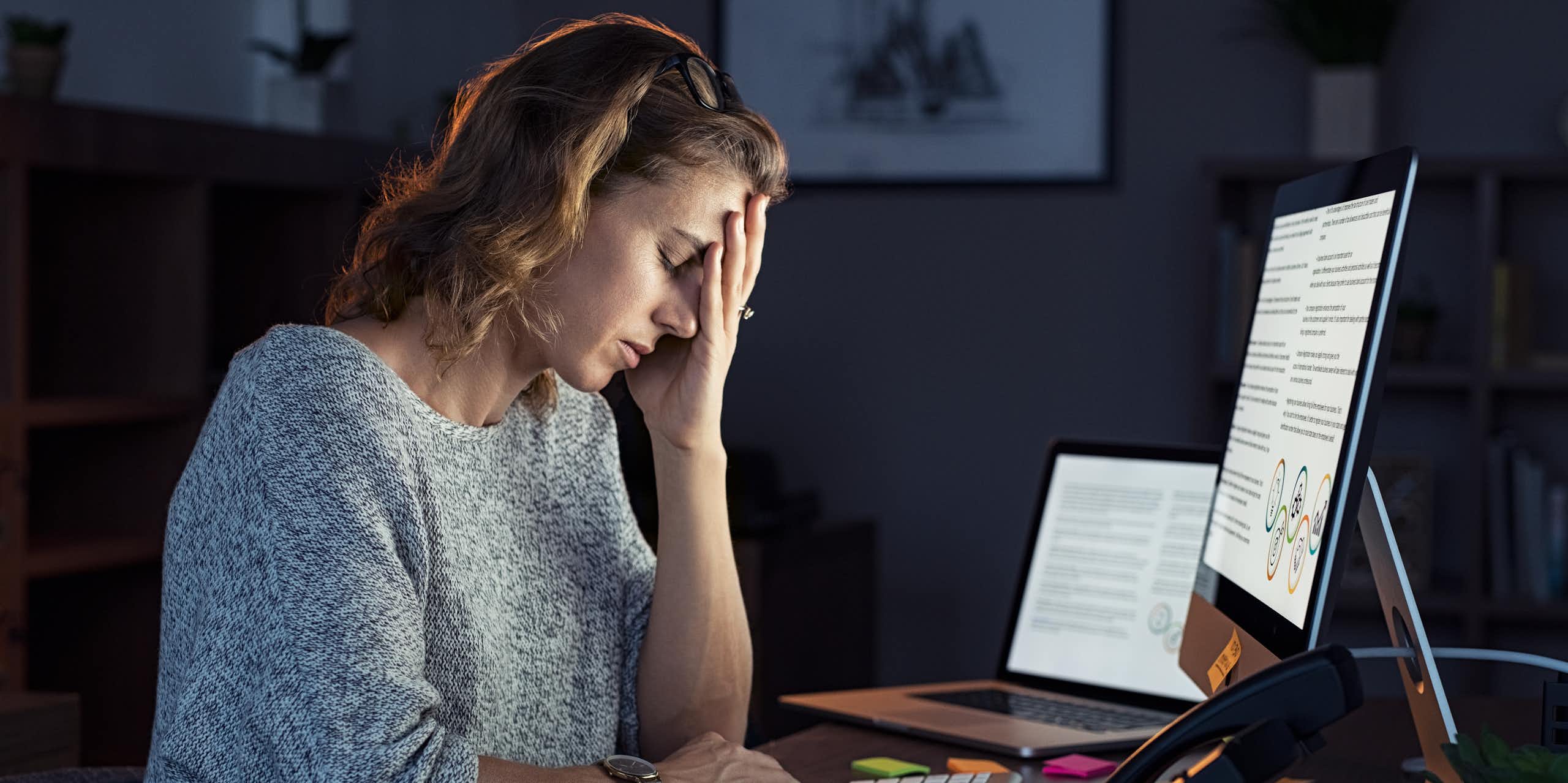 Une femme assise devant un ordinateur à un bureau repose sa tête sur sa main.