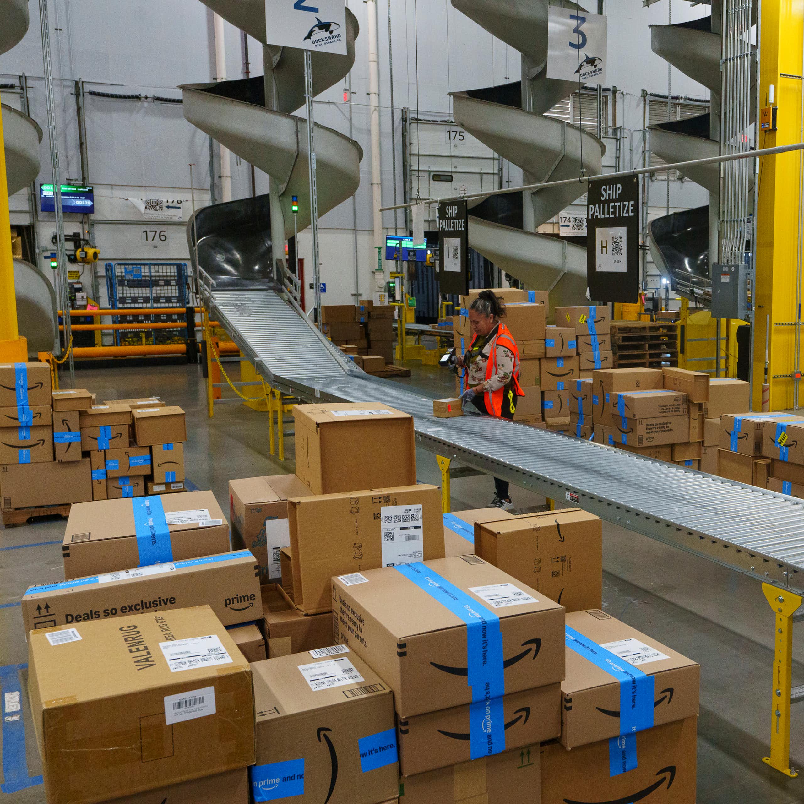 A worker stands by a roller belt in a large warehouse.