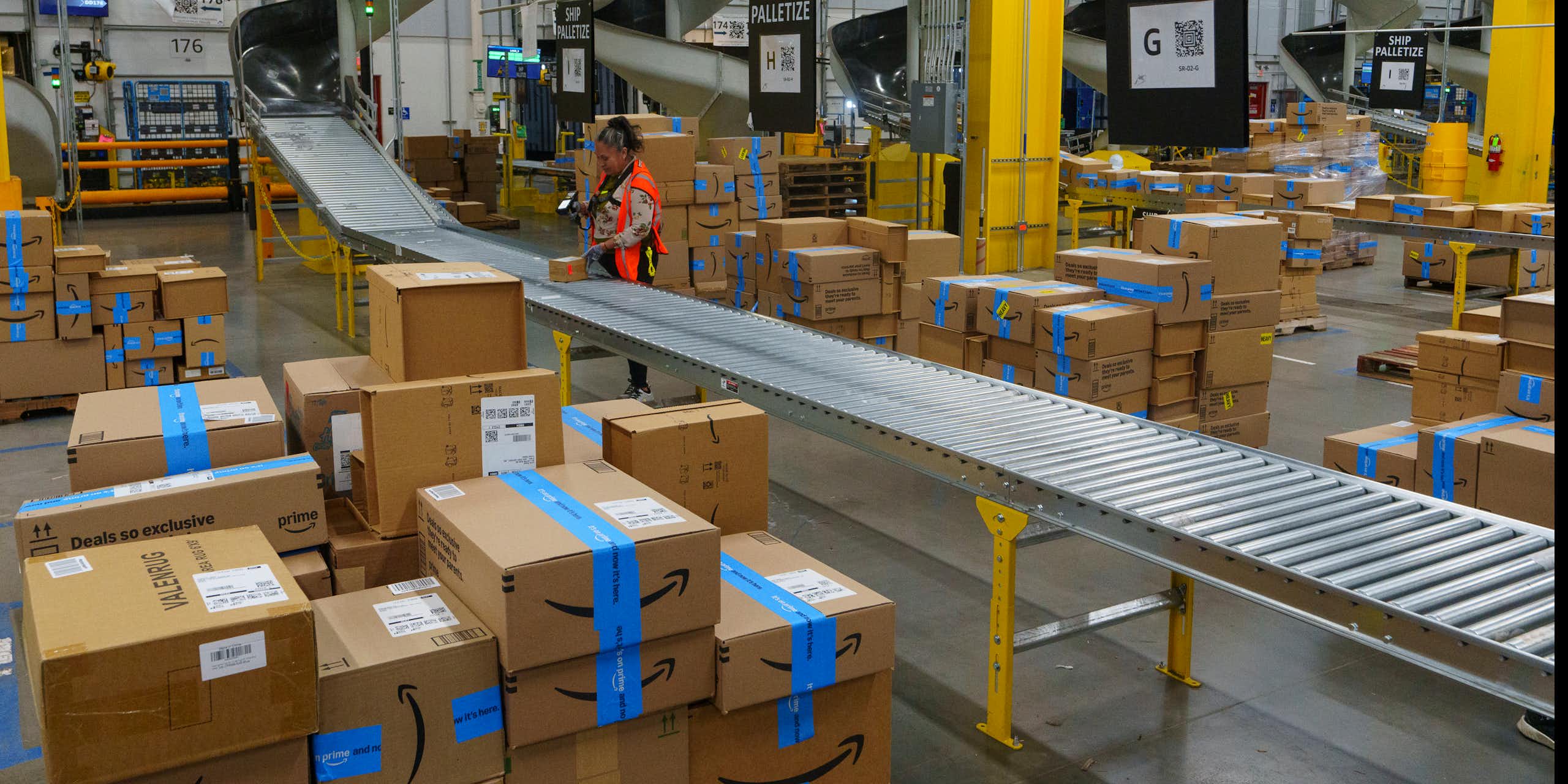 A worker stands by a roller belt in a large warehouse.
