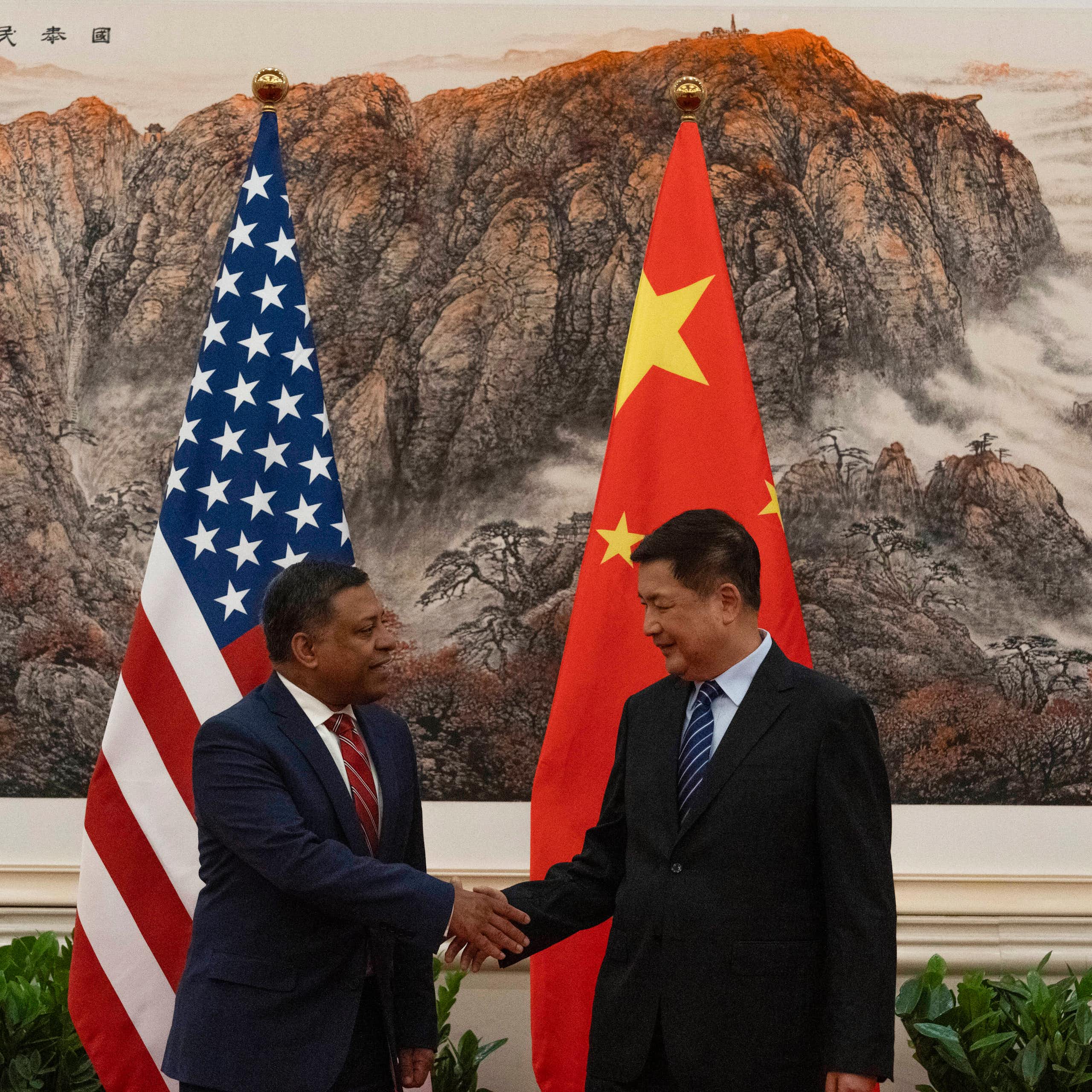 Two men shake hands in front of flags of China and the US