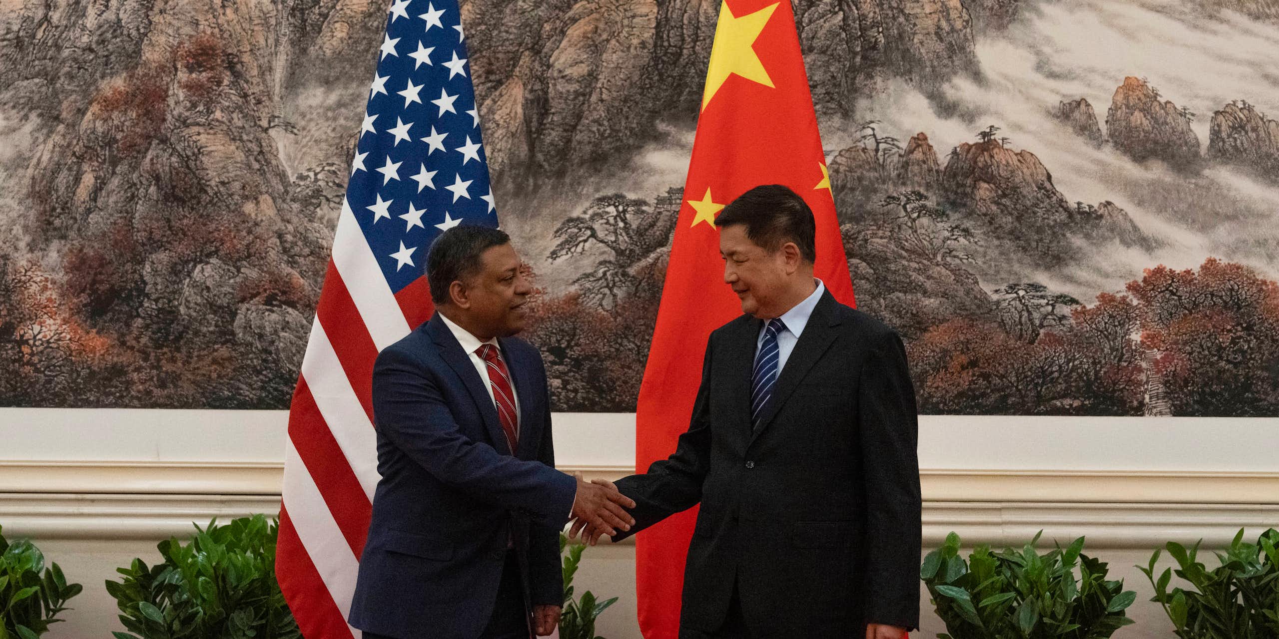 Two men shake hands in front of flags of China and the US