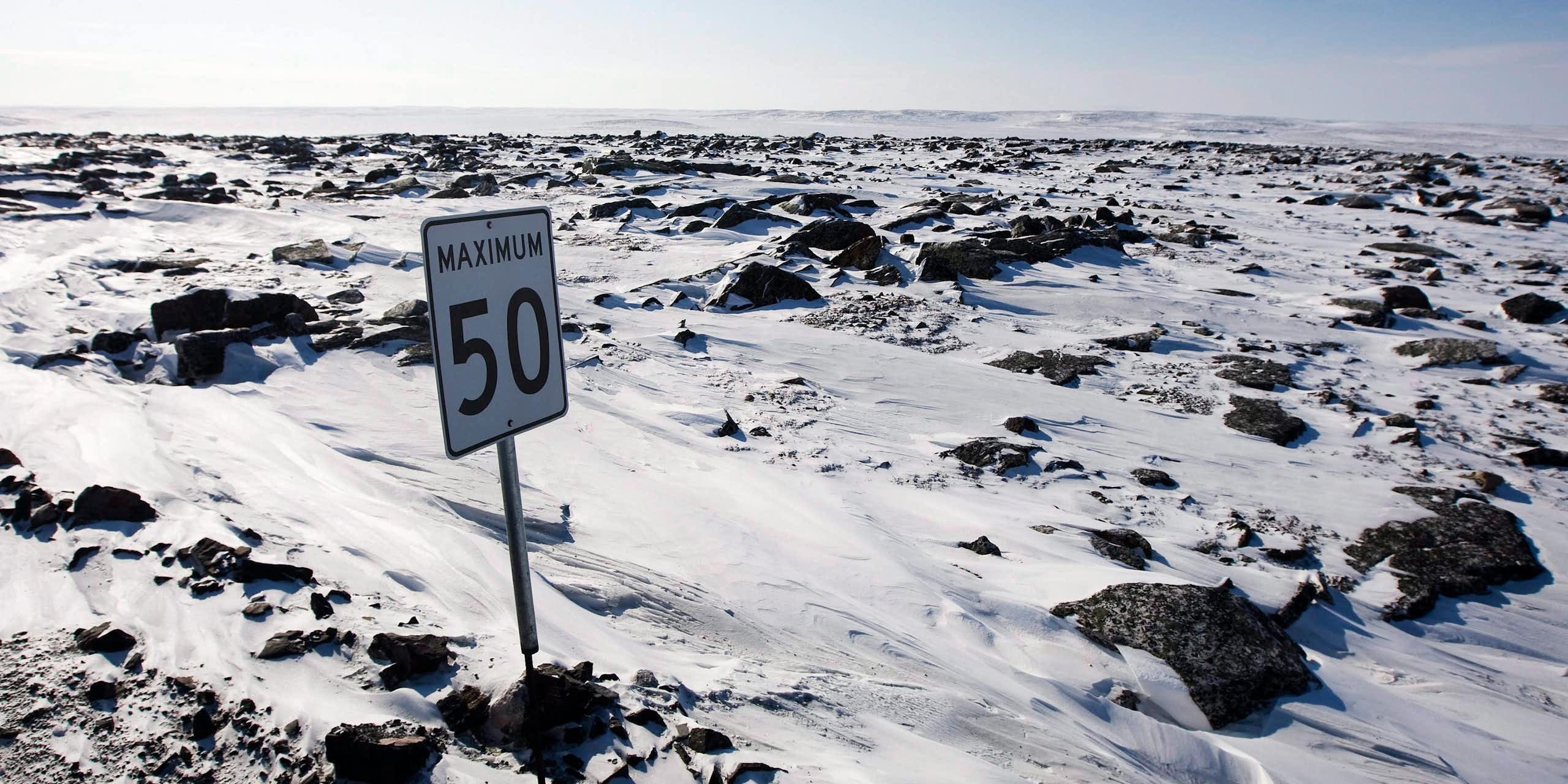 A speed limit sign is seen in a snowy, craggy expanse with no road visible. 