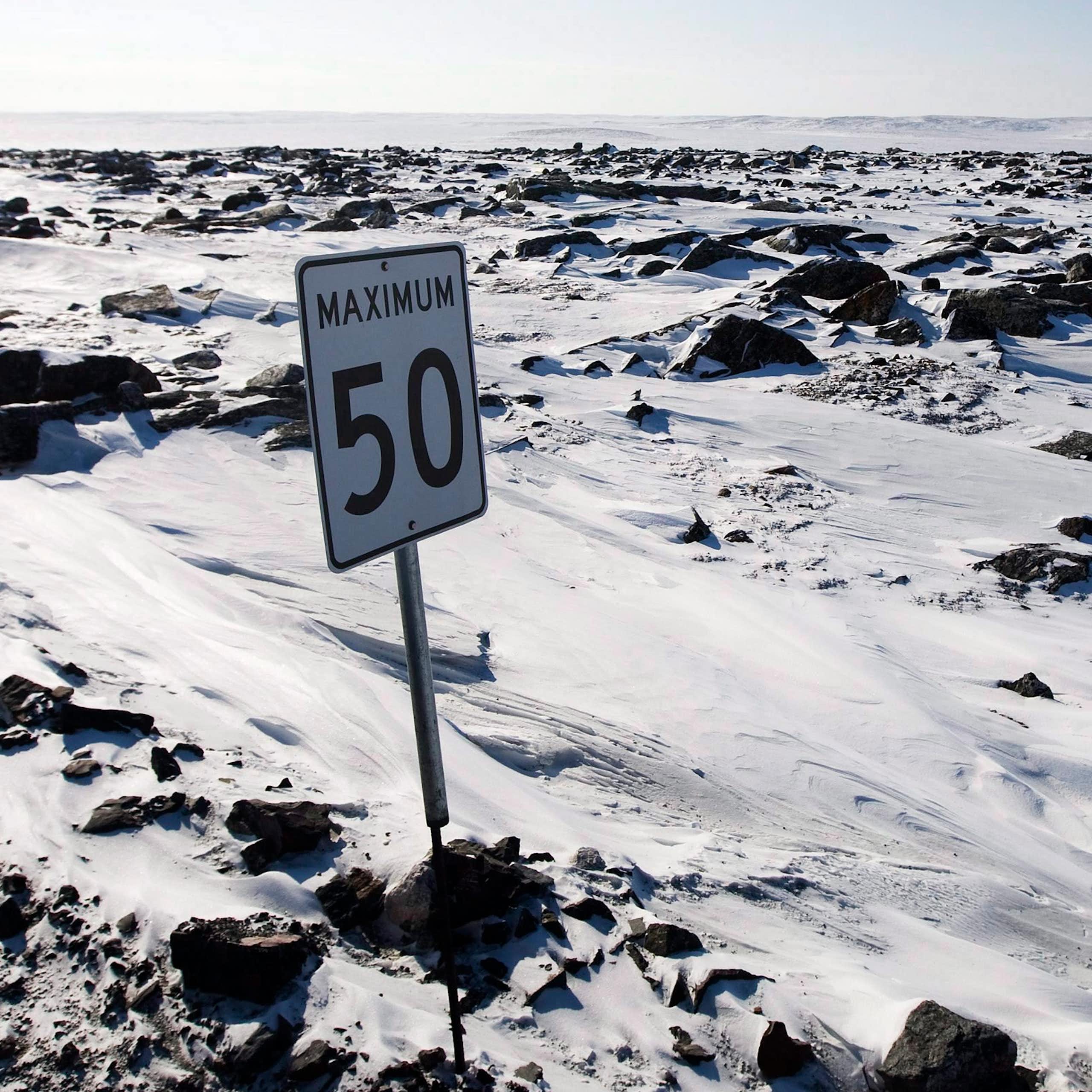 A speed limit sign is seen in a snowy, craggy expanse with no road visible.