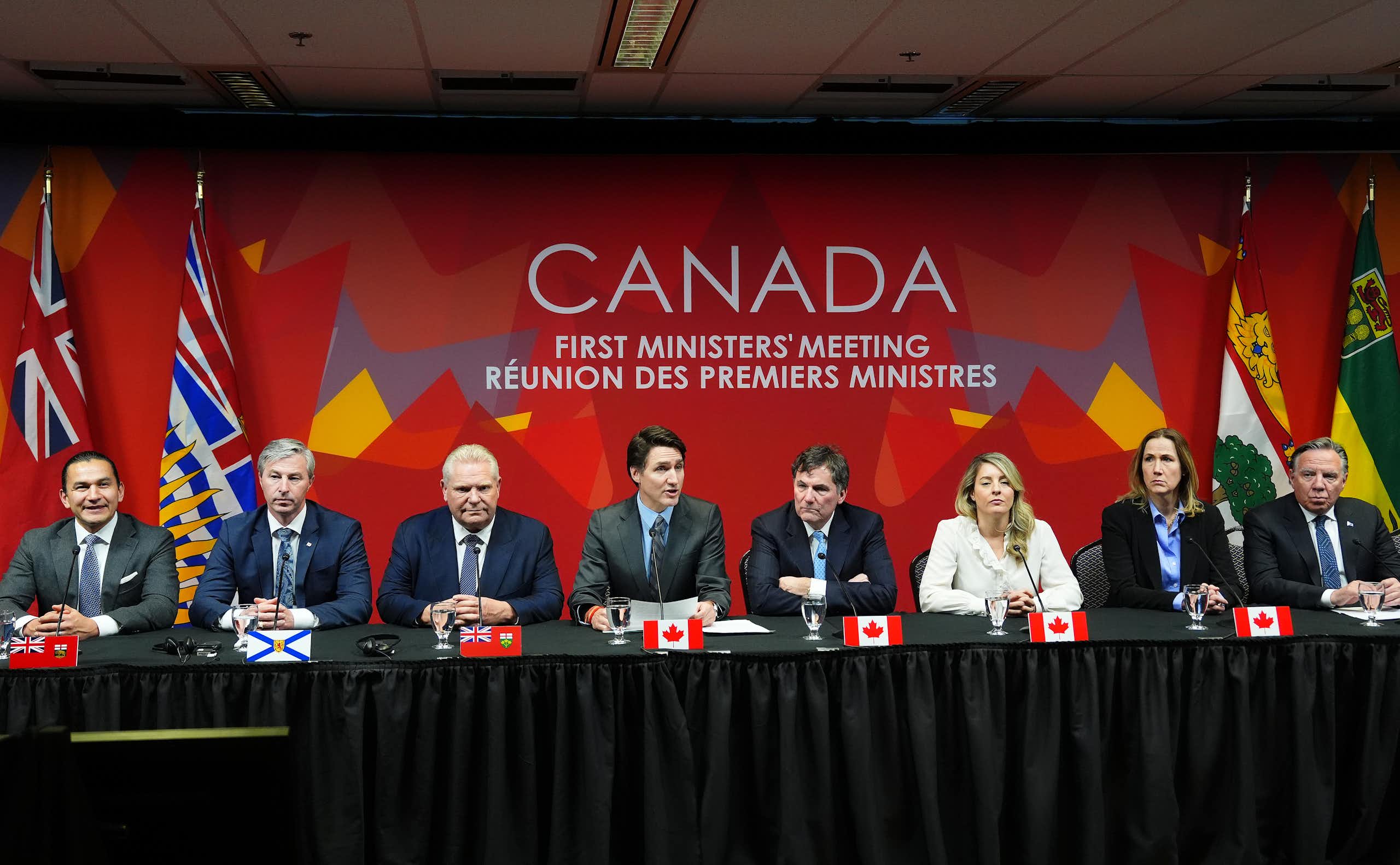 Rangée d'hommes et de femmes assis, avec des drapeaux derrière