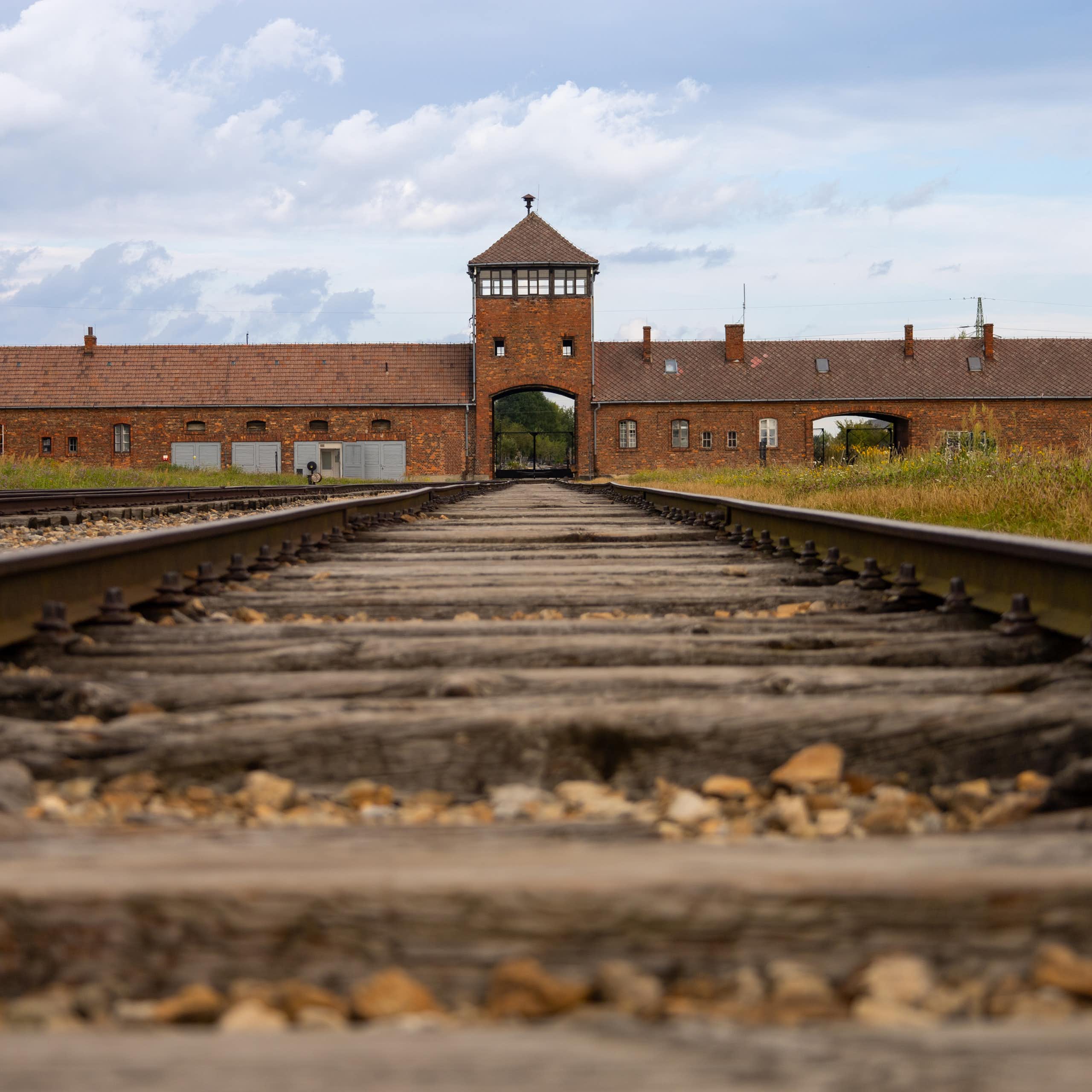 Vue sur une voie ferrée désaffectée, menant à un bâtiment en brique.