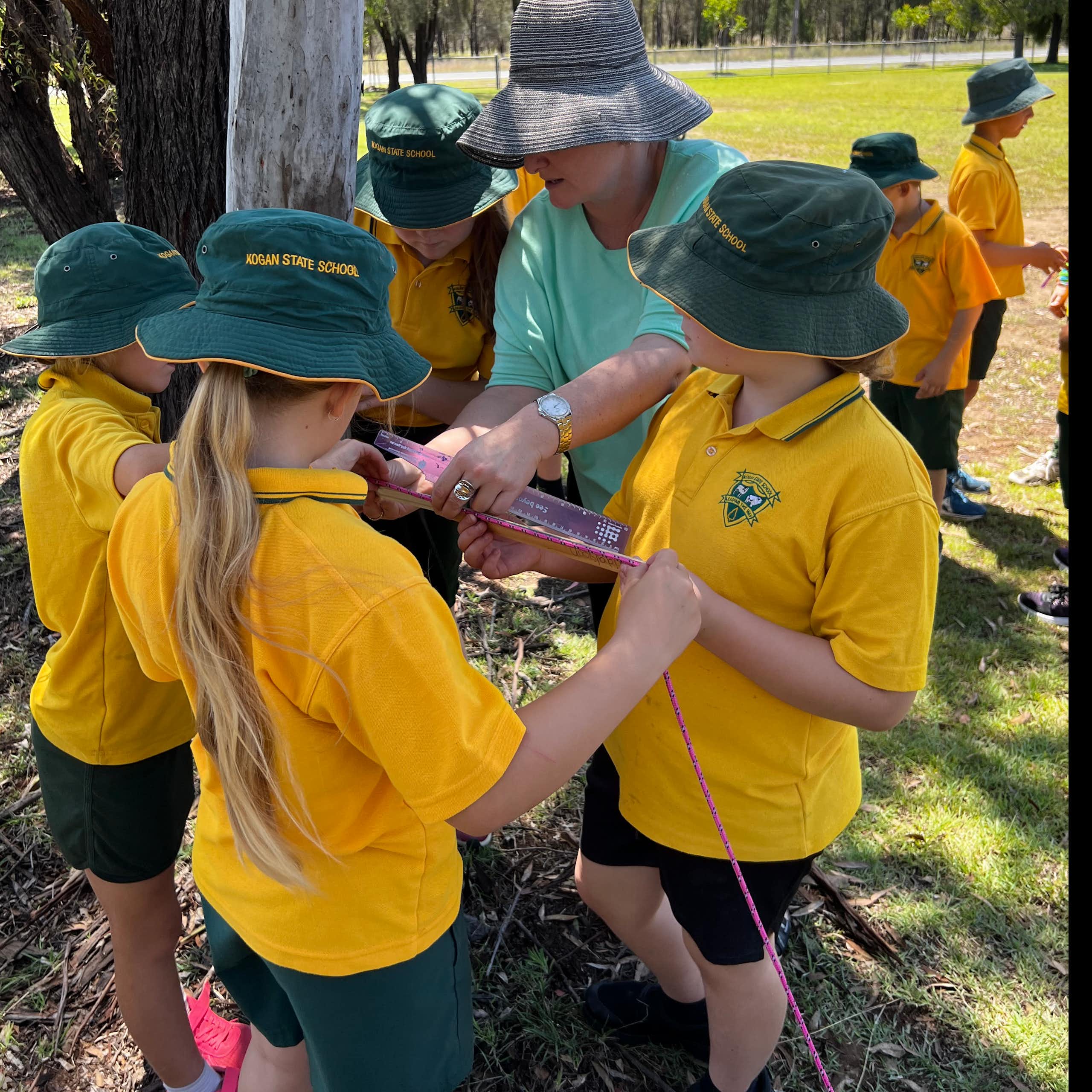 Kids in green hats and yellow tops with teacher outside