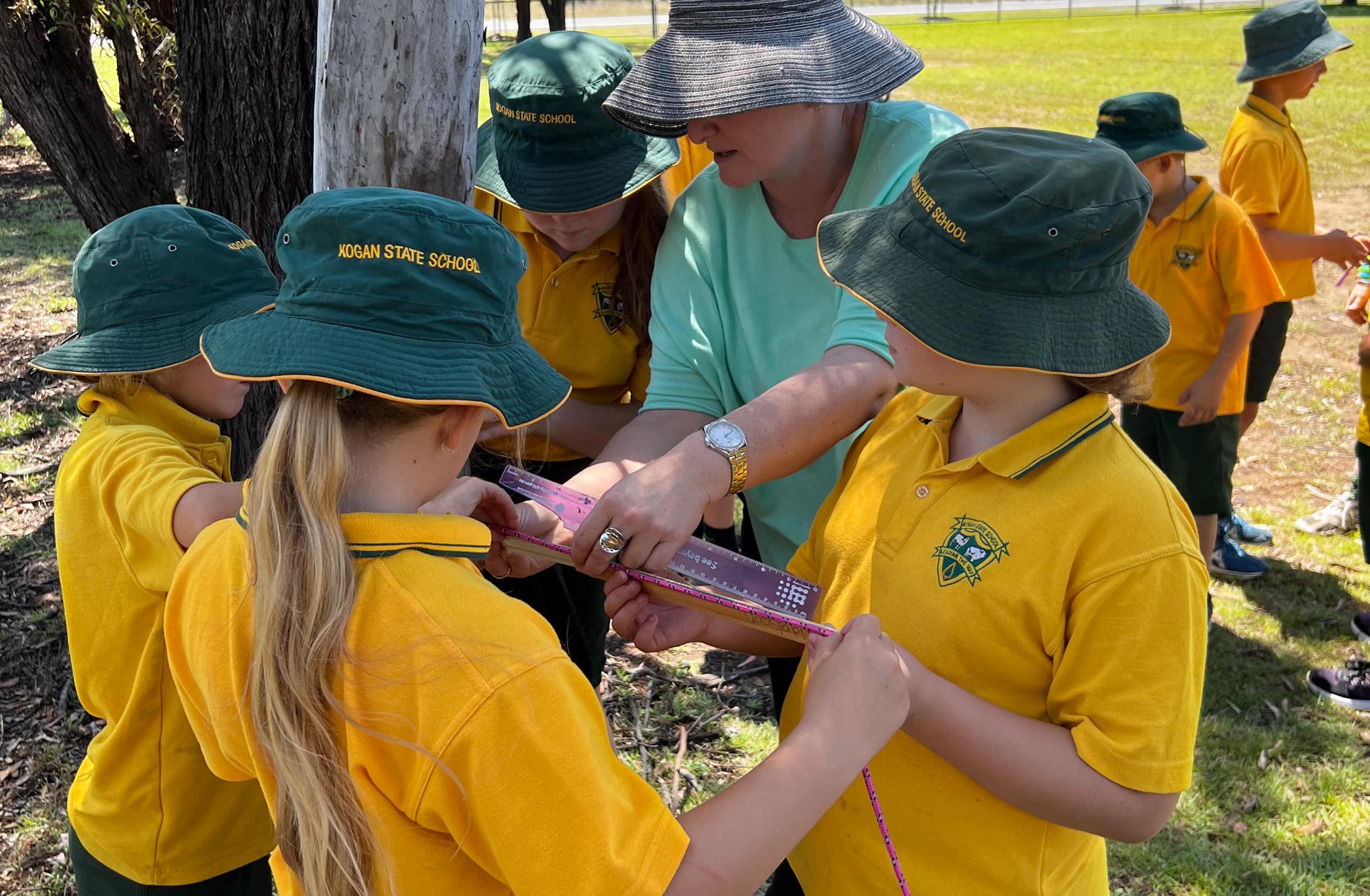 Kids in green hats and yellow tops with teacher outside