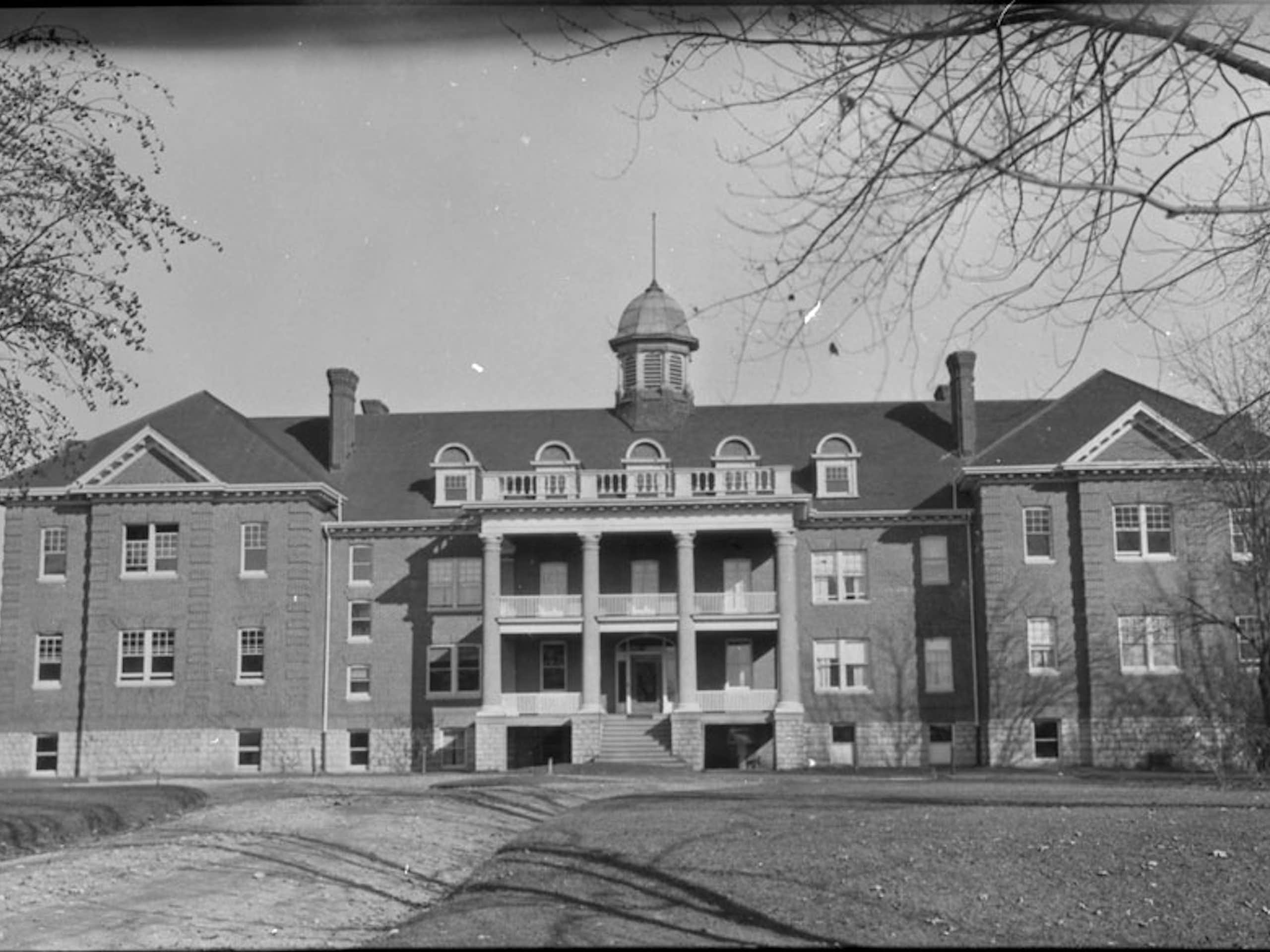 A black and white photo of a large brick building surrounded by trees