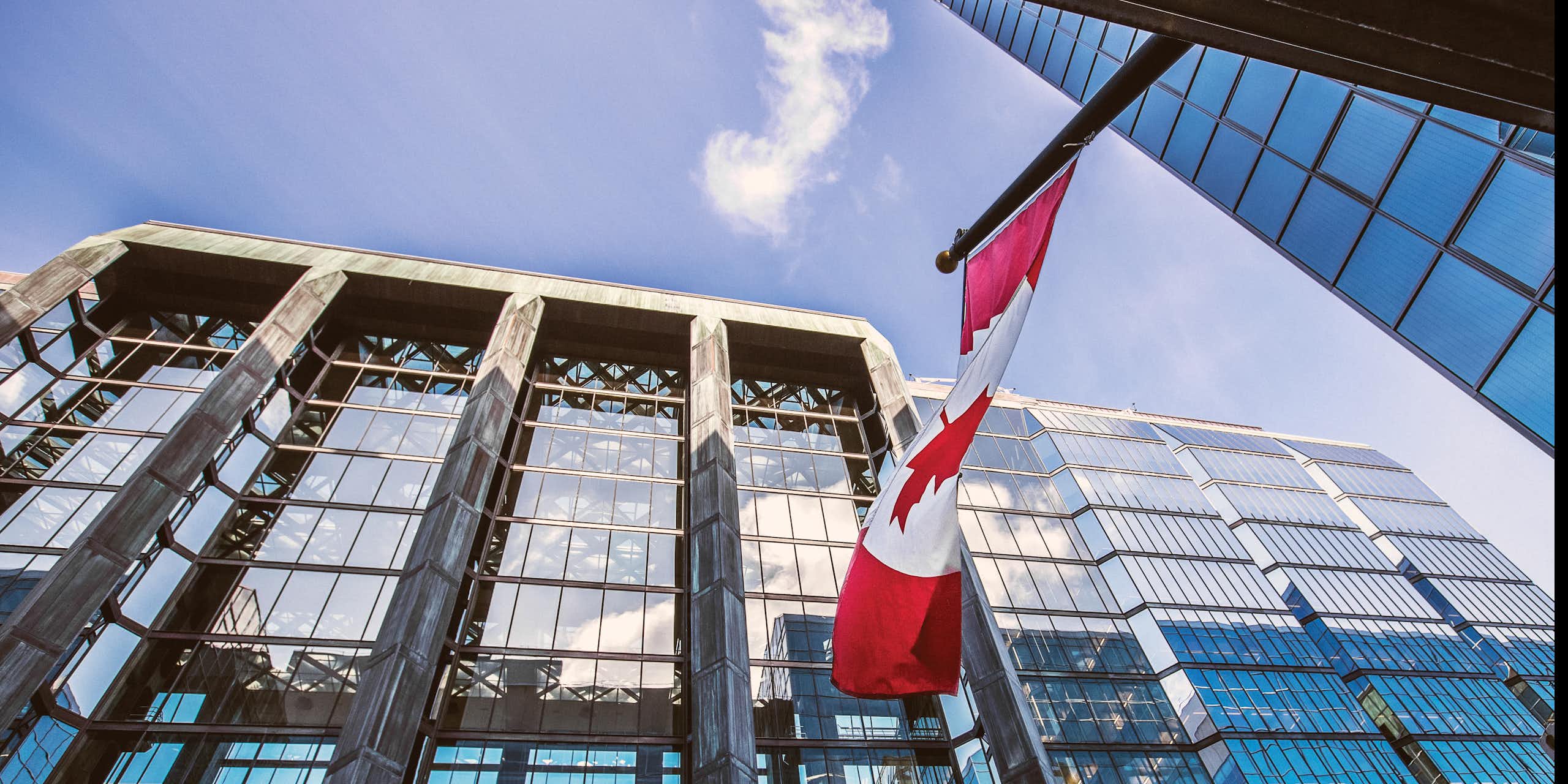 Upward shot of a glass-fronted office building with a Canadian flag flying in front
