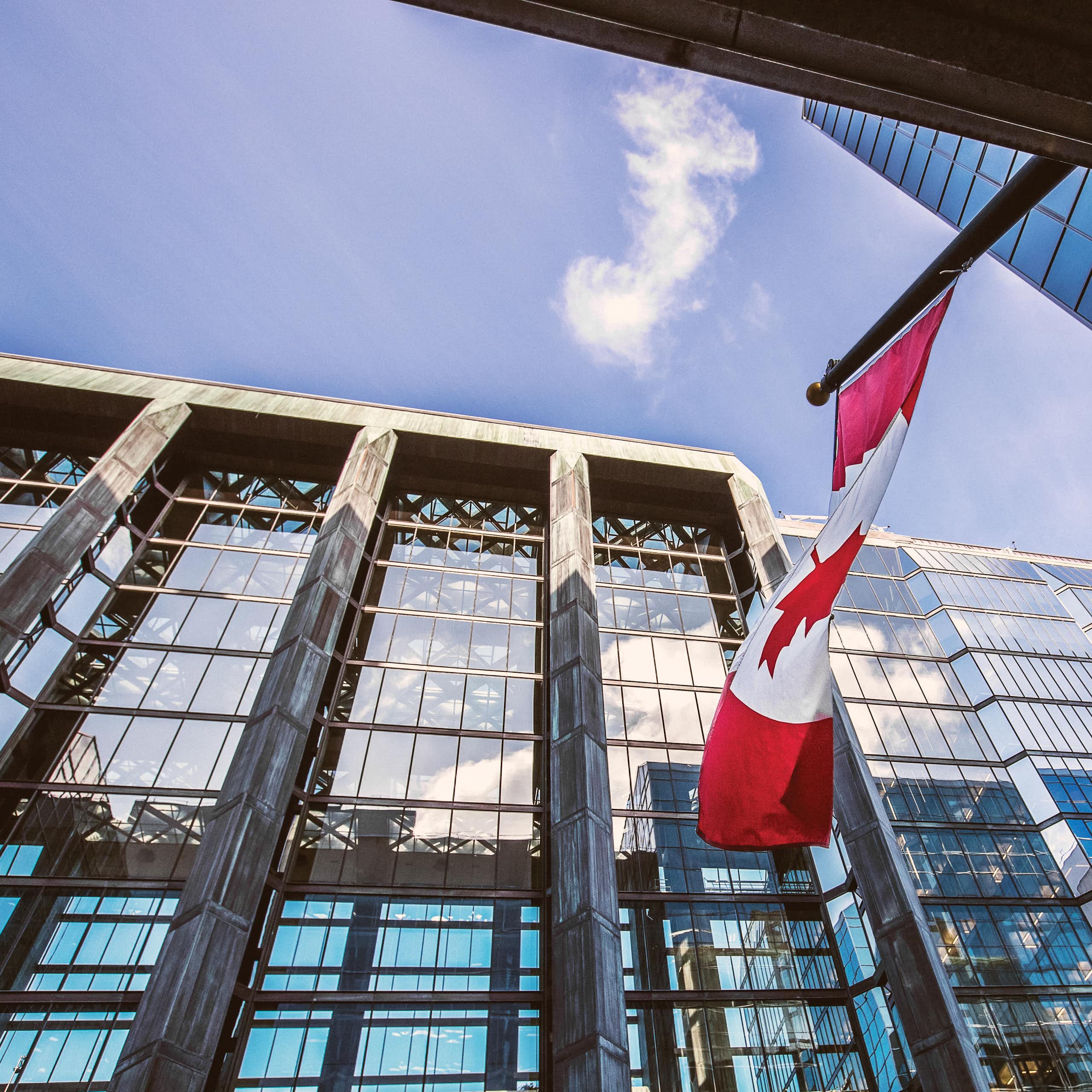 Upward shot of a glass-fronted office building with a Canadian flag flying in front