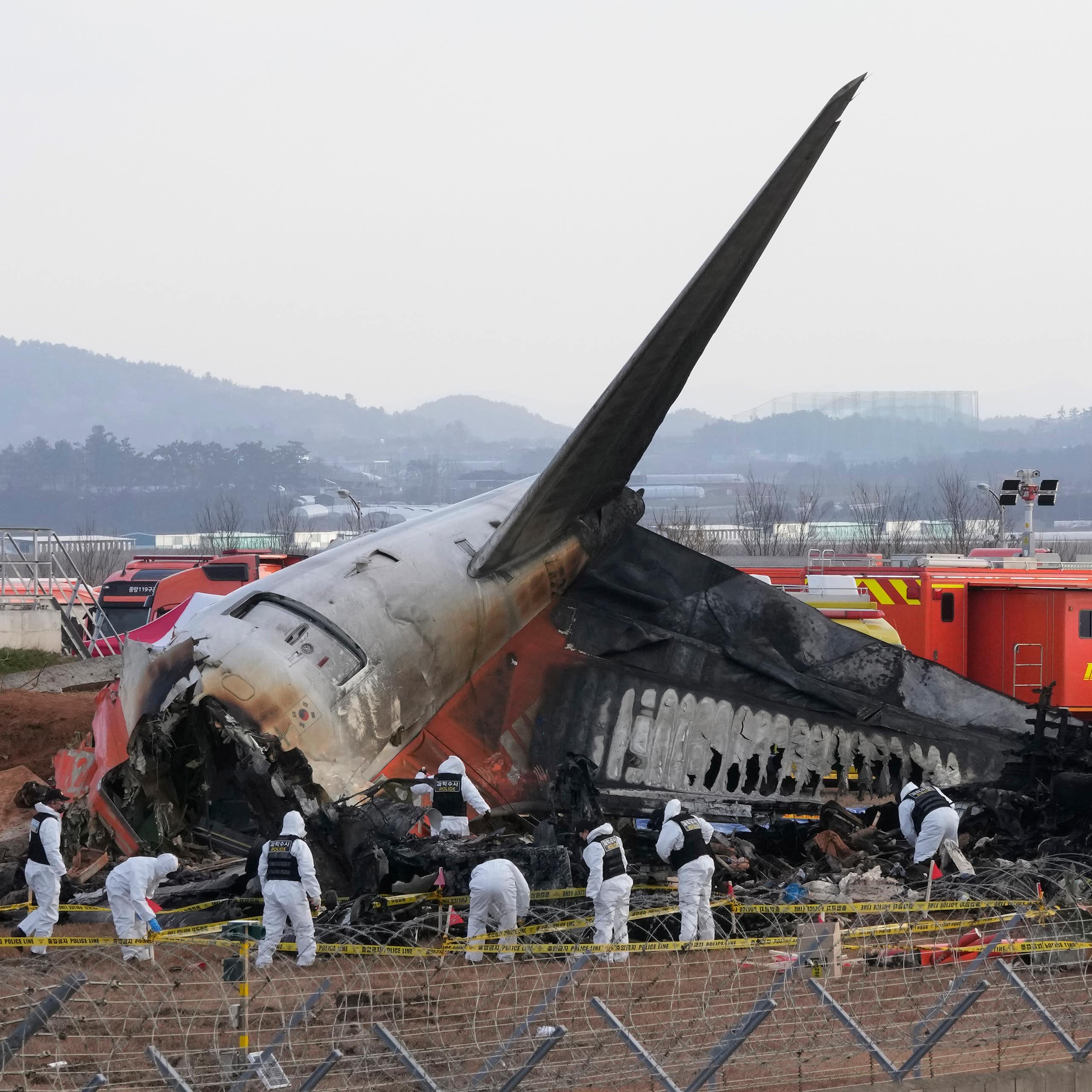 Rescue workers wearing white safety gear work through the wreckage of a burnt plane, which has crashed into the runway at a South Korean airport.