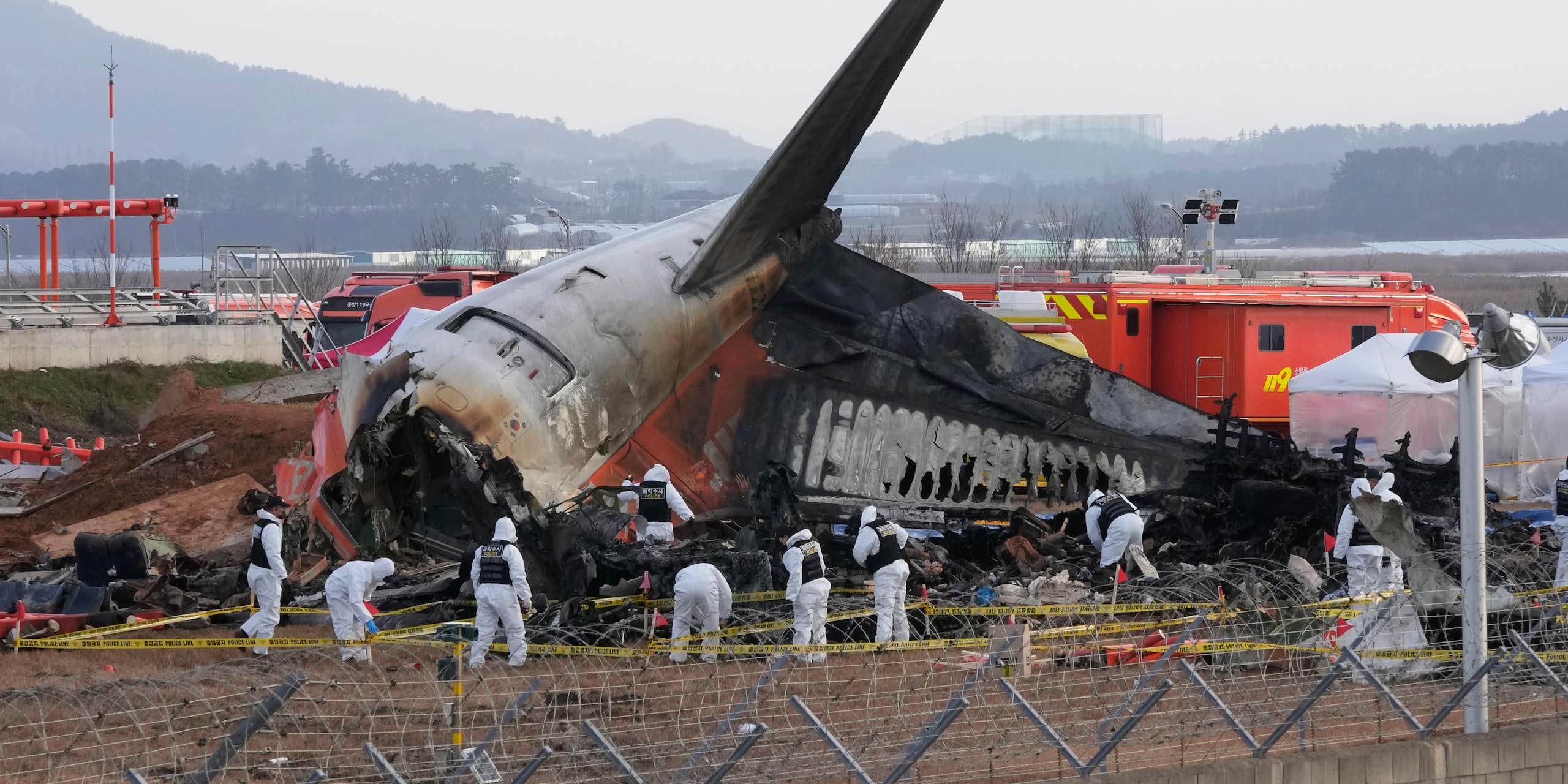 Rescue workers wearing white safety gear work through the wreckage of a burnt plane, which has crashed into the runway at a South Korean airport.