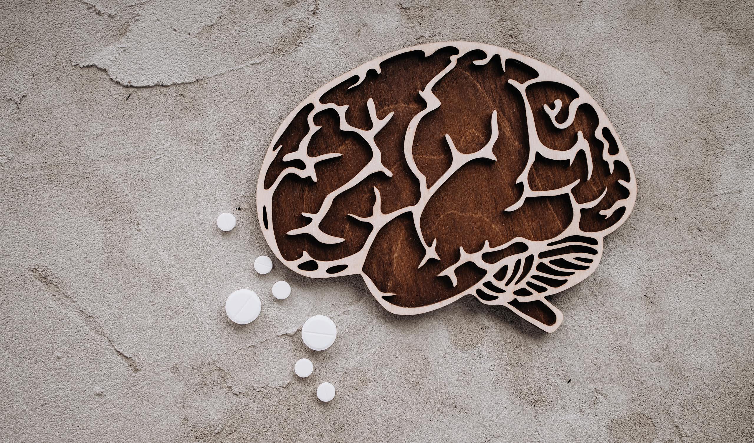 Wooden cutout of a human brain and several white tablets of different sizes