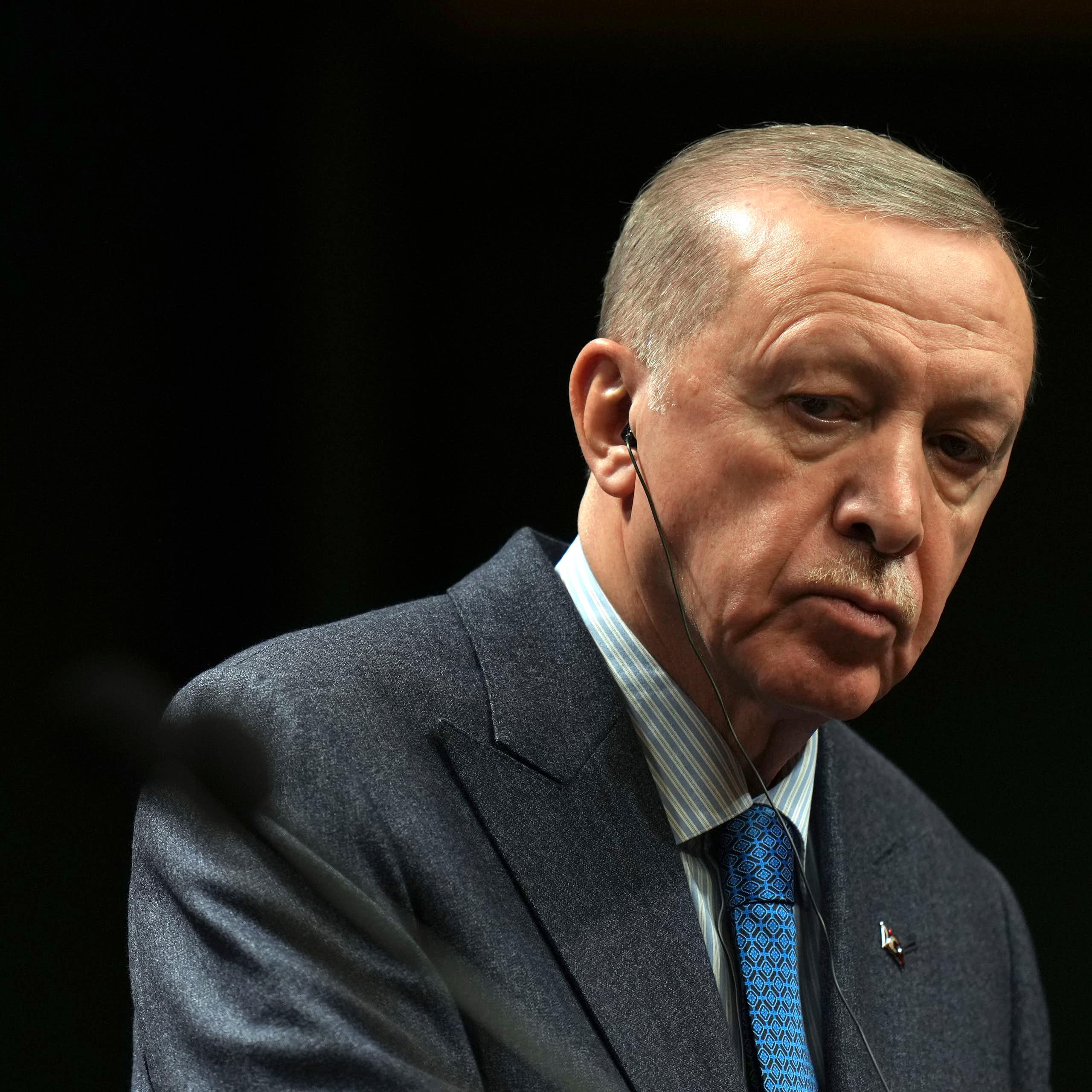 A man with thin grey hair listens while a bearded man, out of focus, speaks.