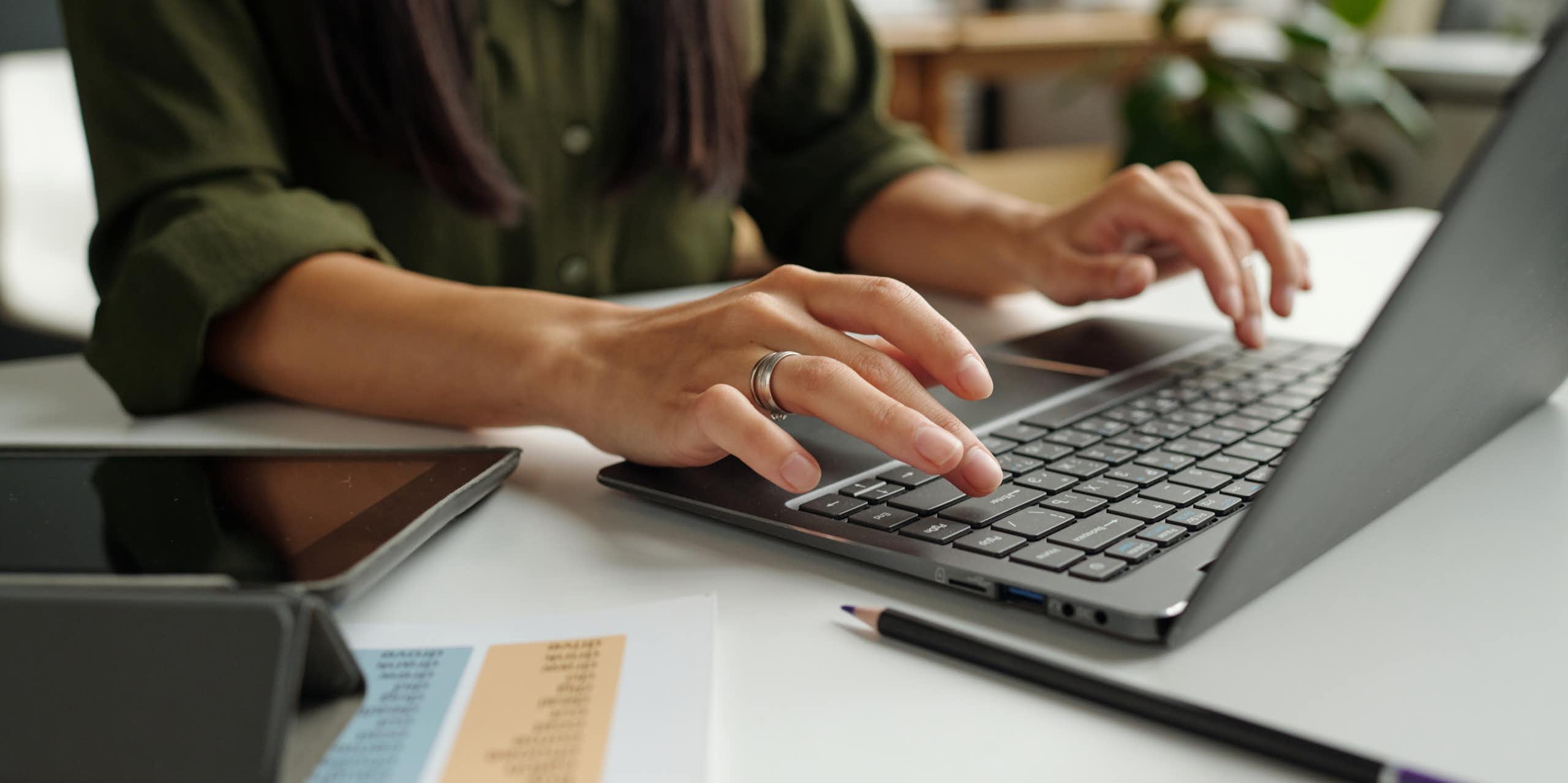 A person seen from the shoulders down typing on a laptop