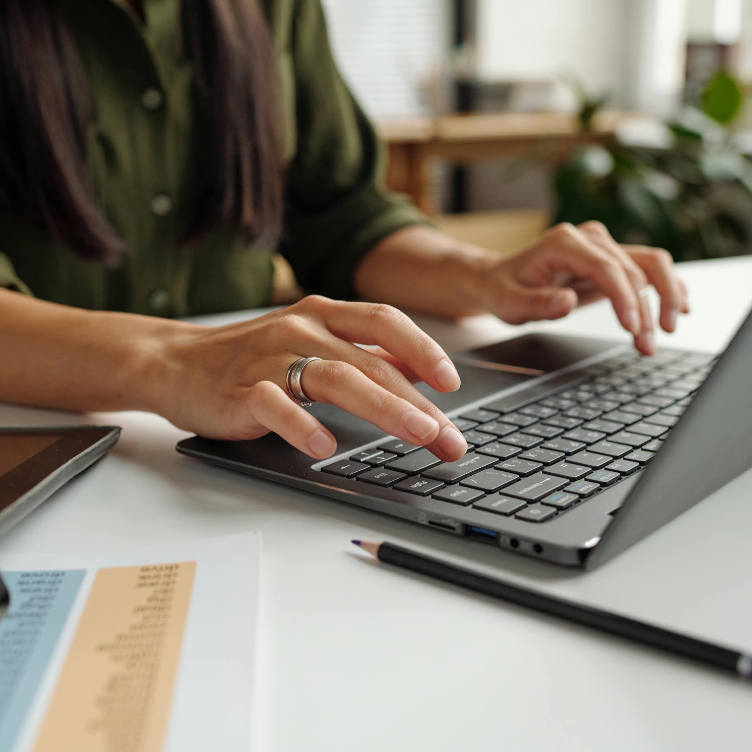 A person seen from the shoulders down typing on a laptop