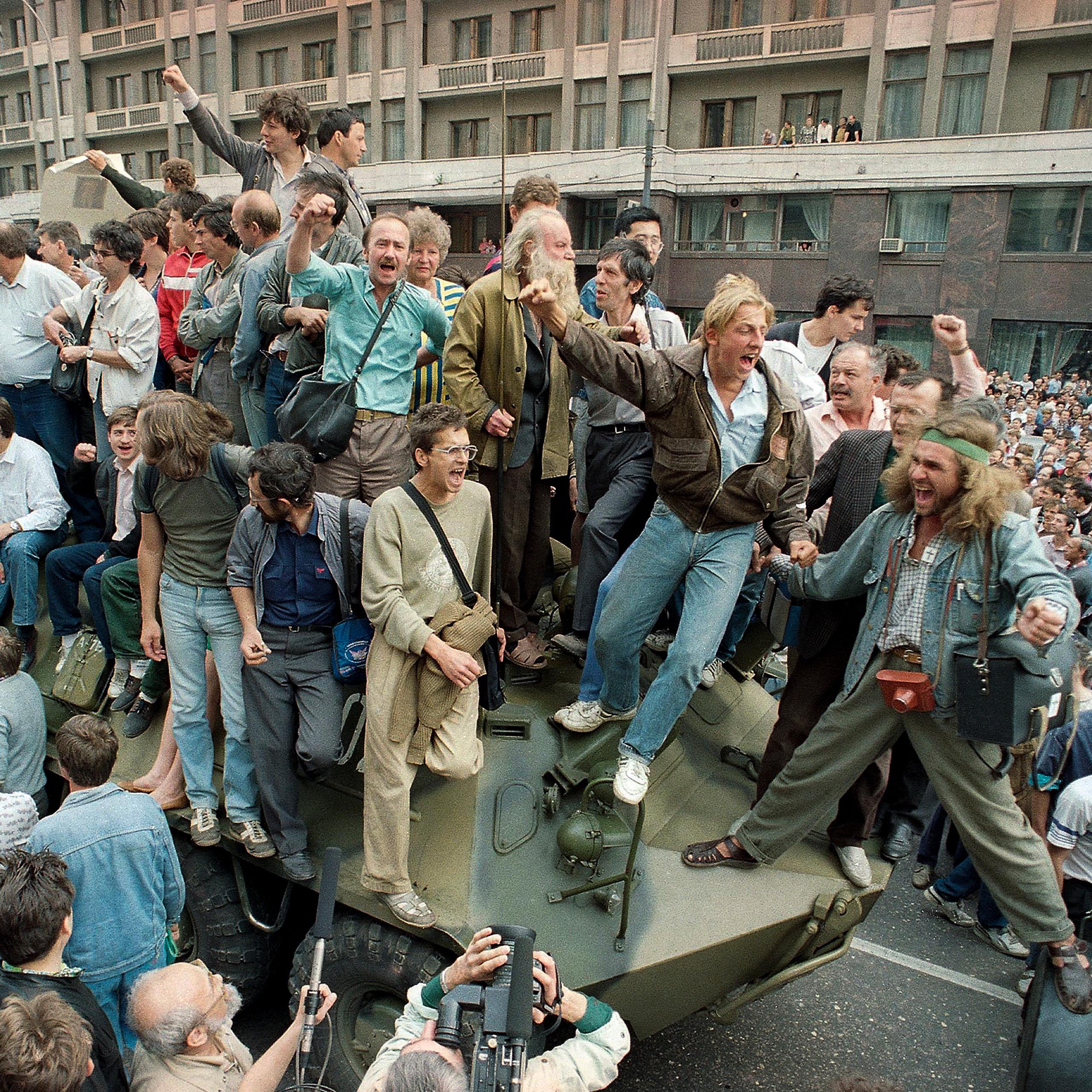 Des personnes en liesse entourent un véhicule militaire et montent dessus.