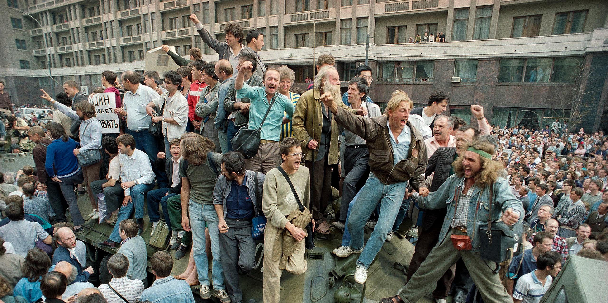 Des personnes en liesse entourent un véhicule militaire et montent dessus.