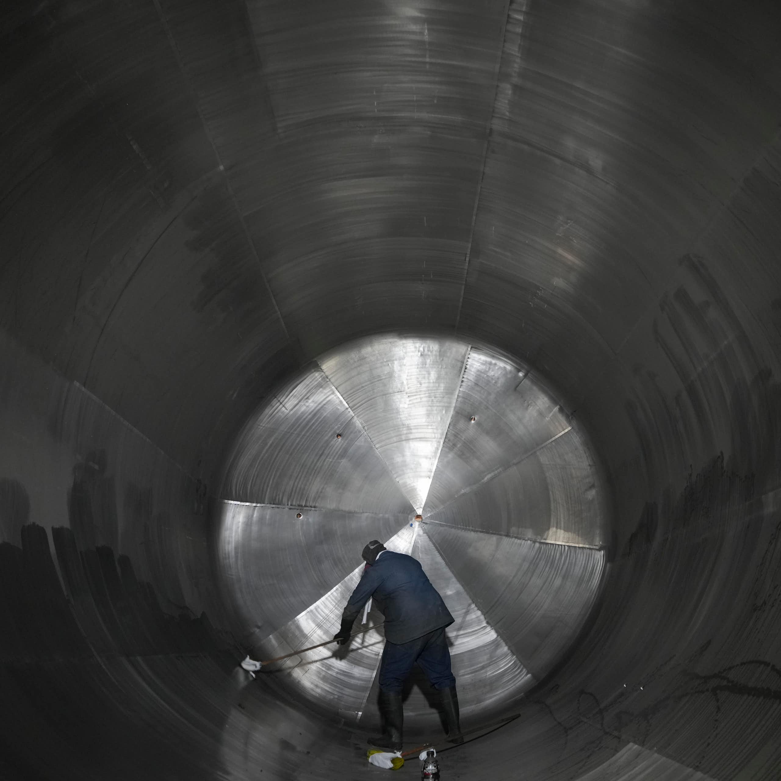 A man cleans the inside of a massive cylindrical steel tank