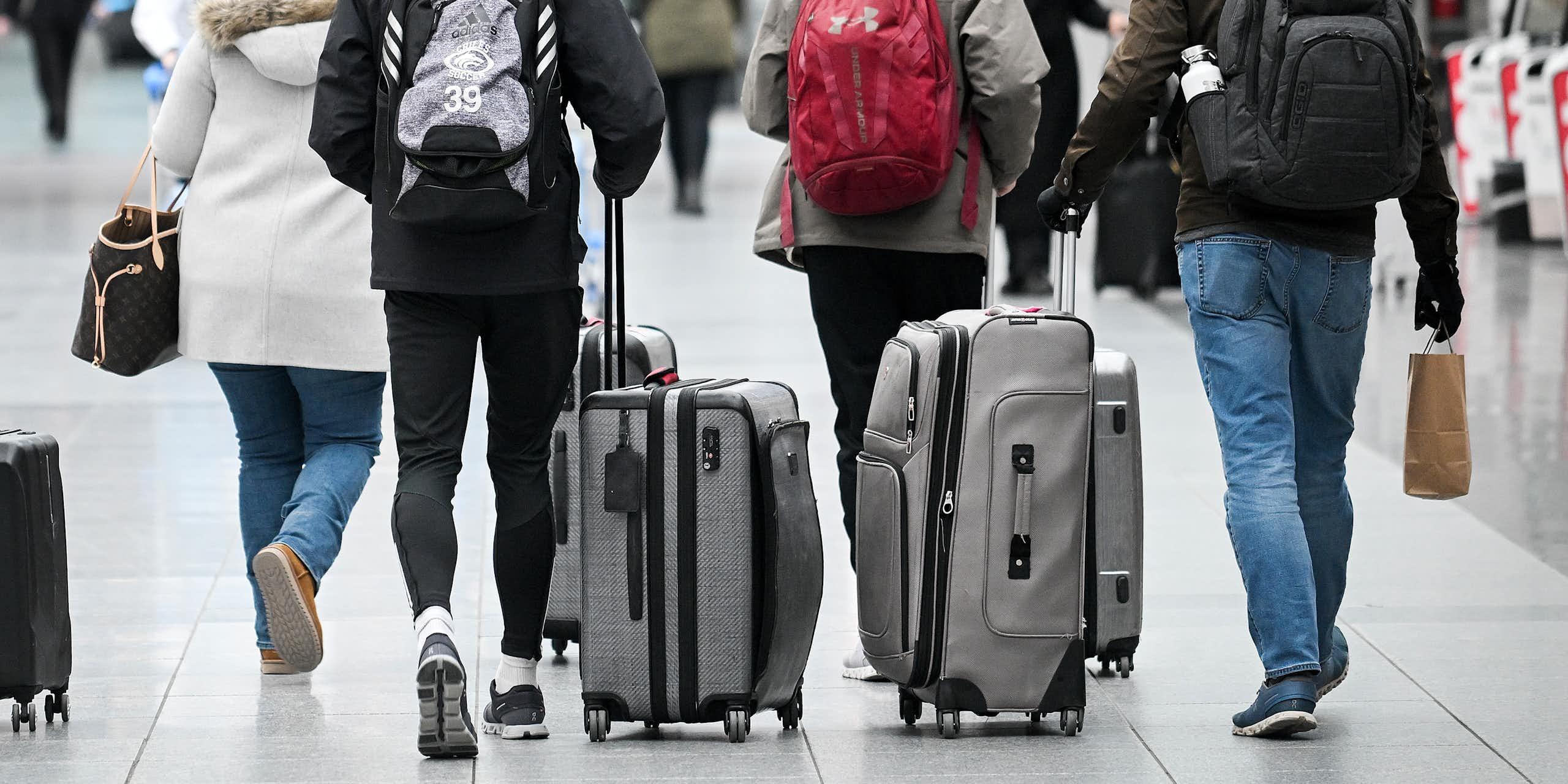 People, seen from behind, walk through an airport wheeling luggage