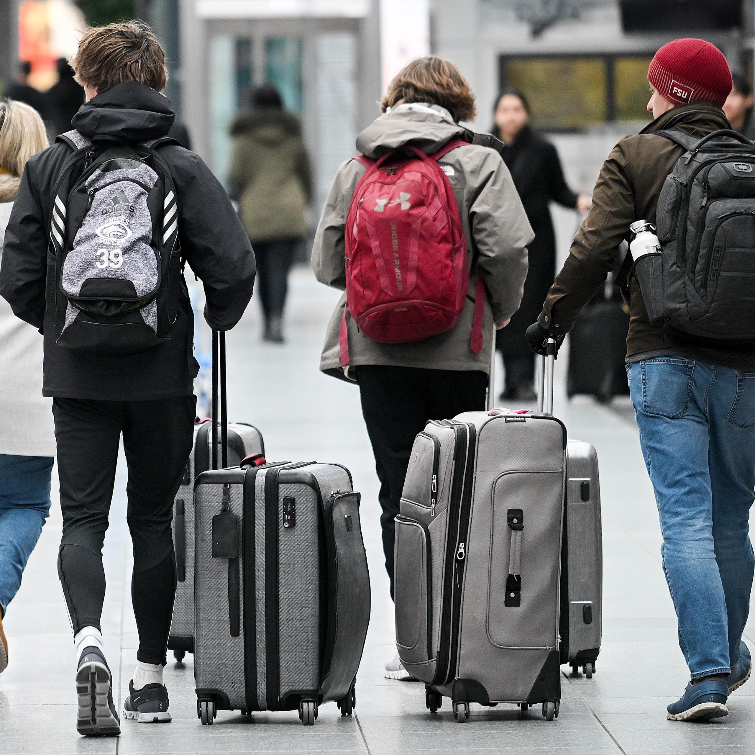 People, seen from behind, walk through an airport wheeling luggage