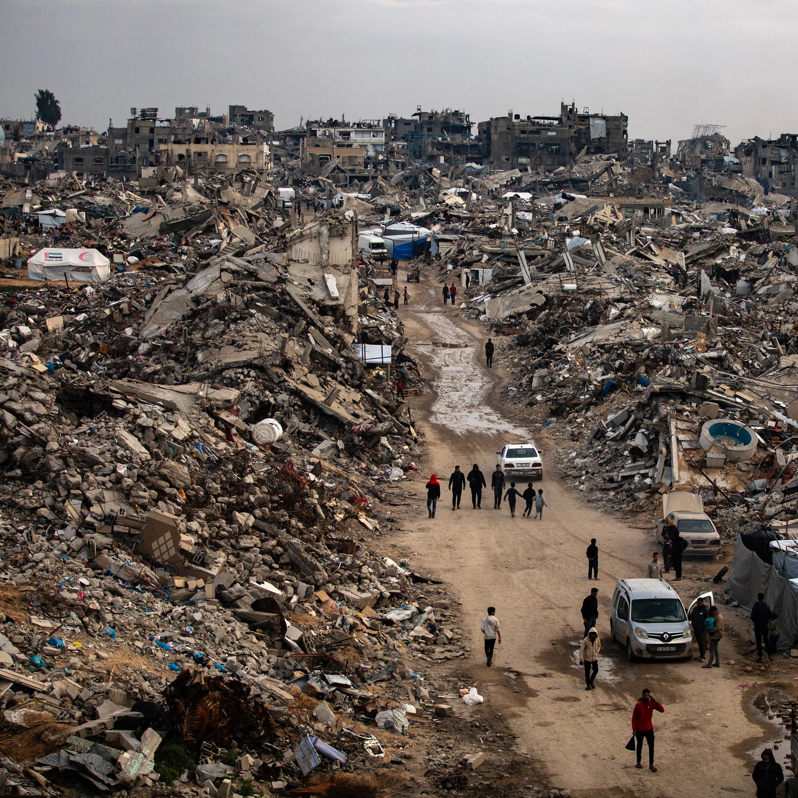 Palestinians walk among the rubble of a destroyed city.
