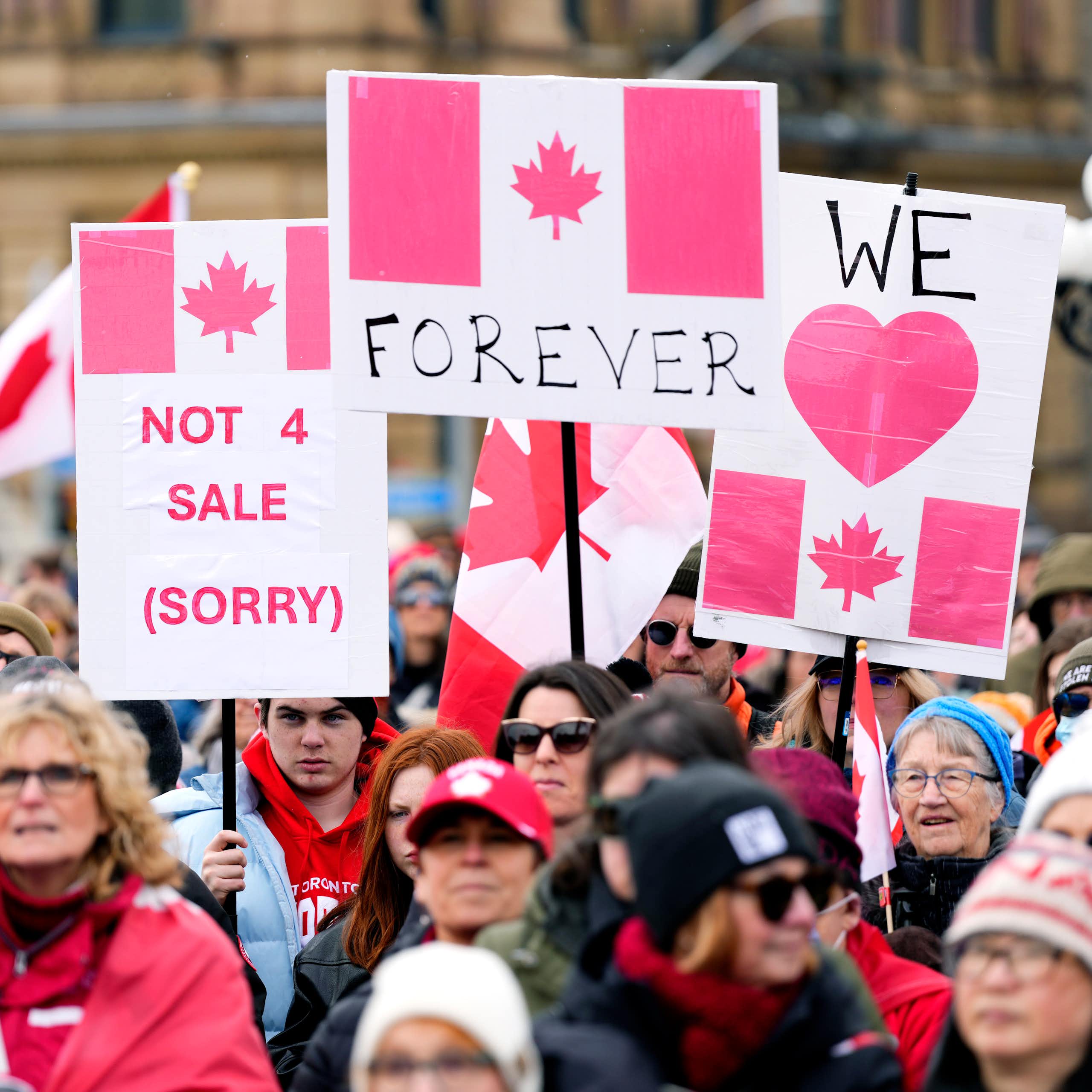 A crowd of protestors. Some of the people hold protest signs that state "Canada not 4 sale," "Canada Forever" and "We love Canada".