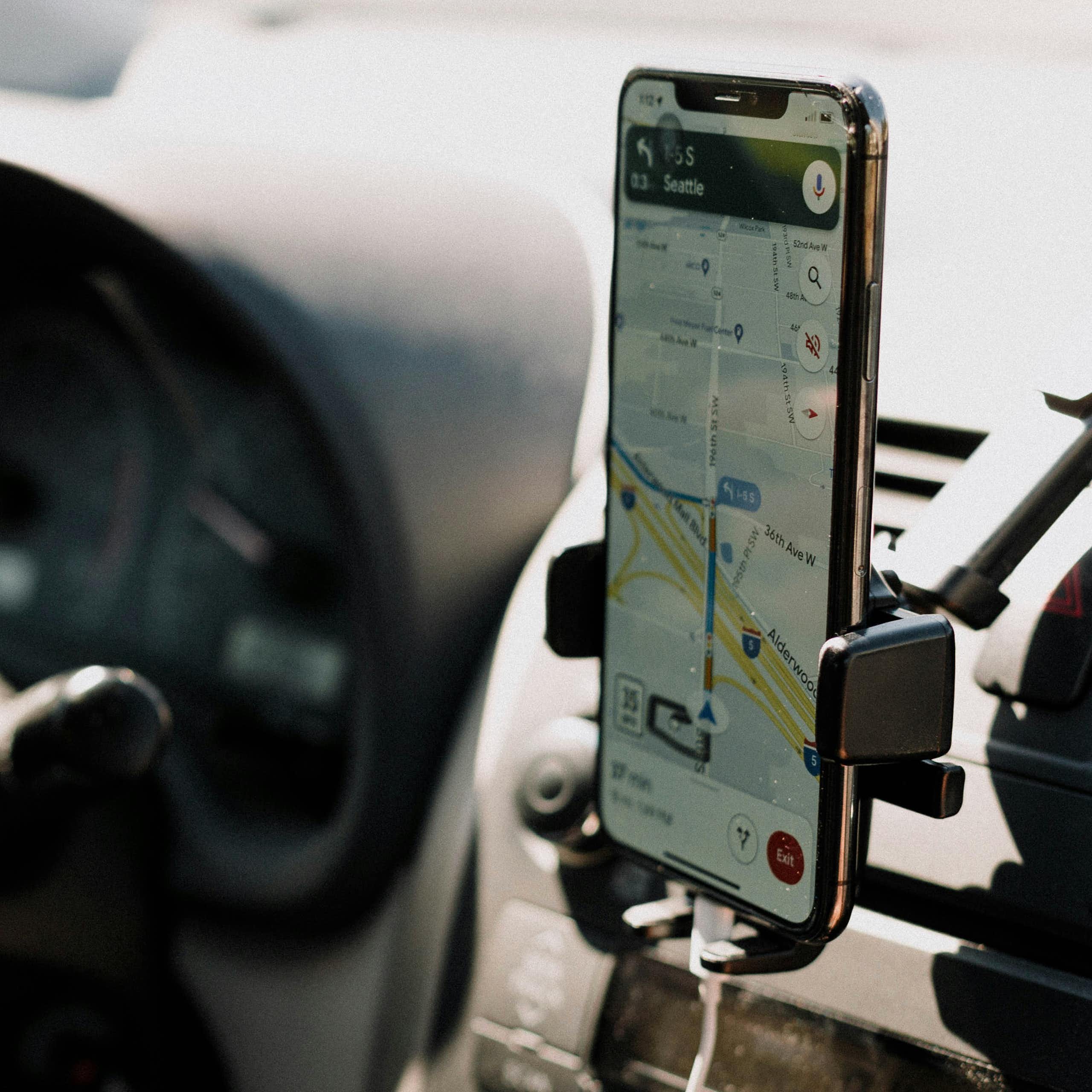 Someone drives a car with their phone on display showing Google Maps.