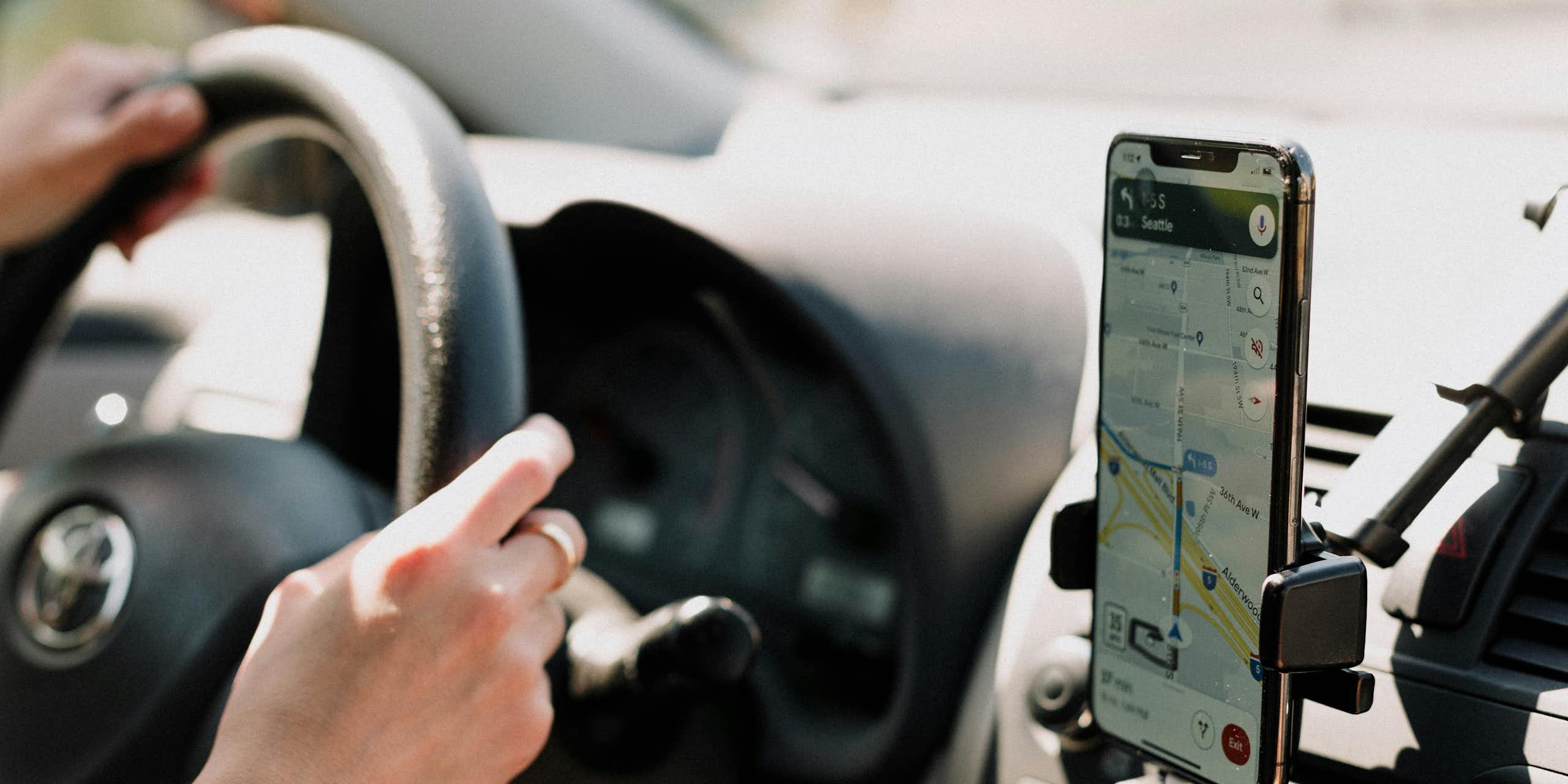 Someone drives a car with their phone on display showing Google Maps.