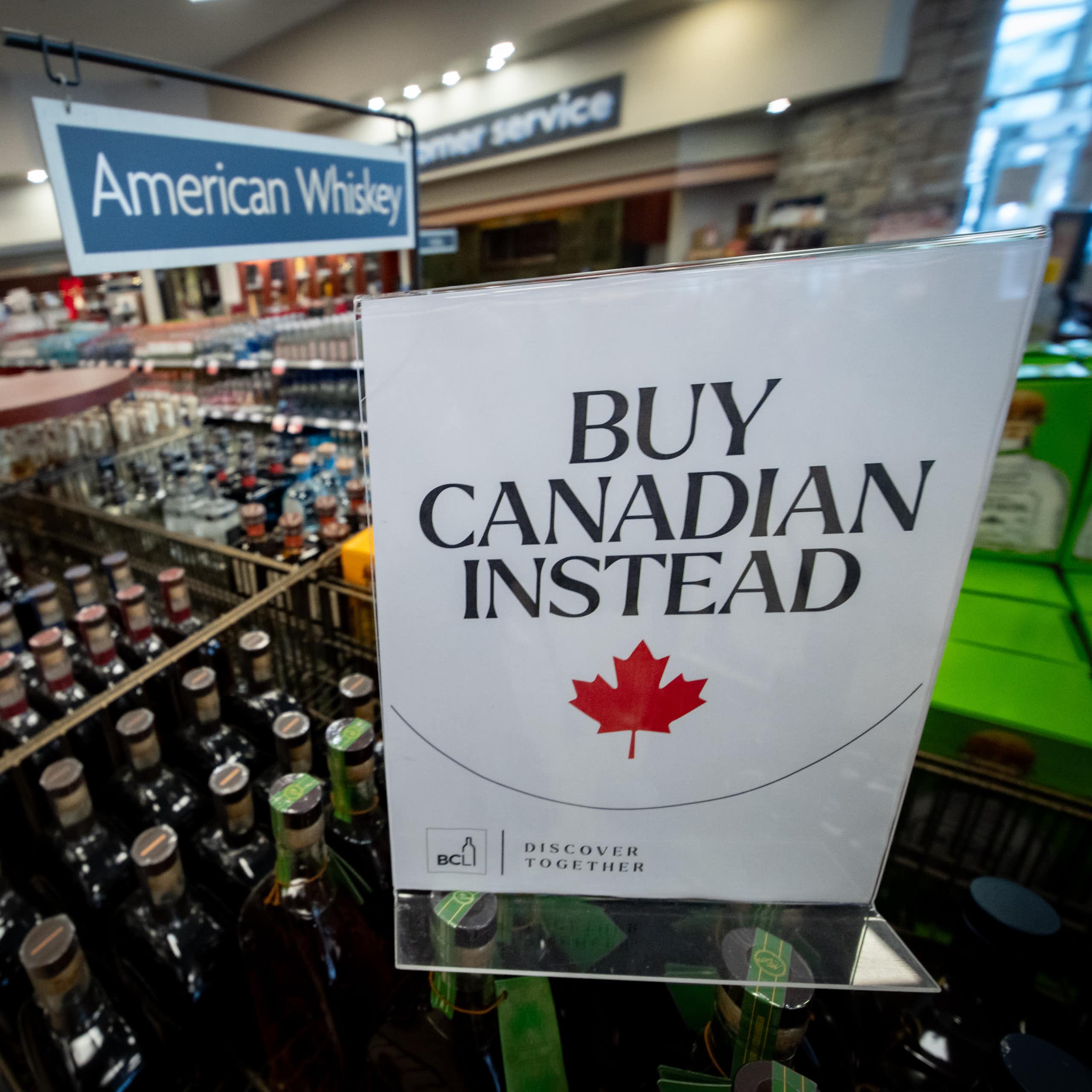 A sign in a liquor store that reads "Buy Canadian Instead". It has been placed in front of bottles of American whiskey.