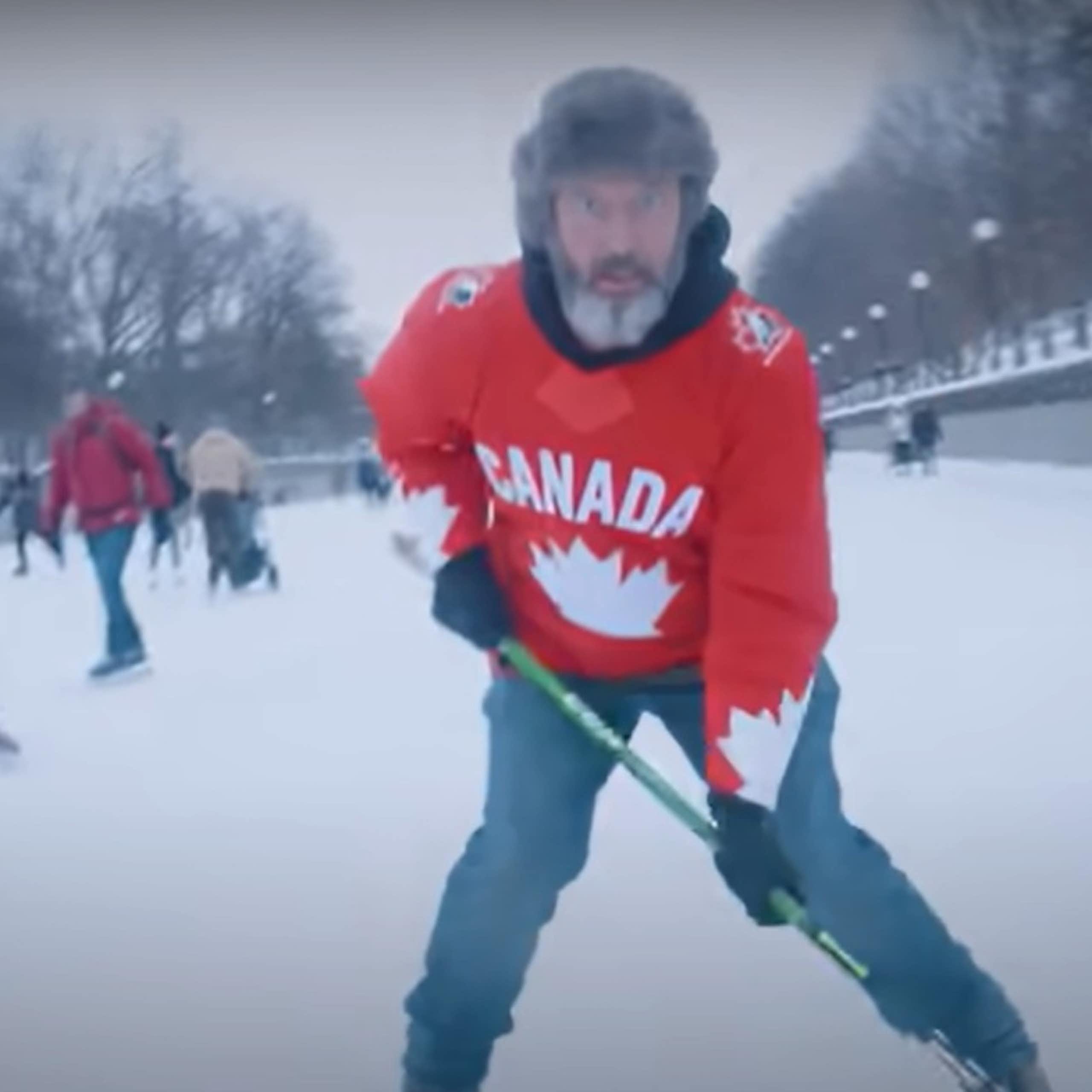 A man in fur hat with a Canada hockey sweater and a hockey stick skating.