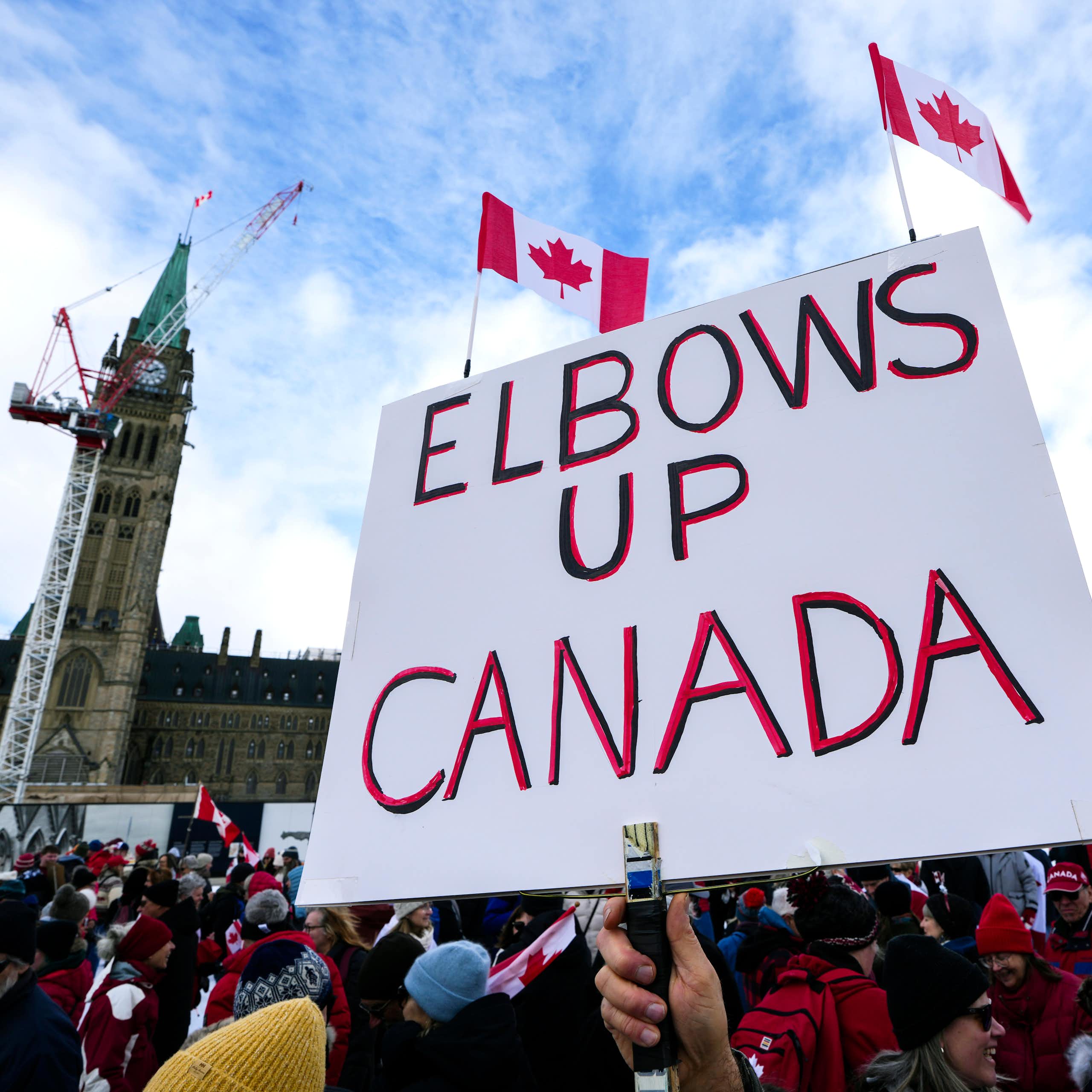 A person holding a white placard reading elbows up canada with two small canadian flags attached