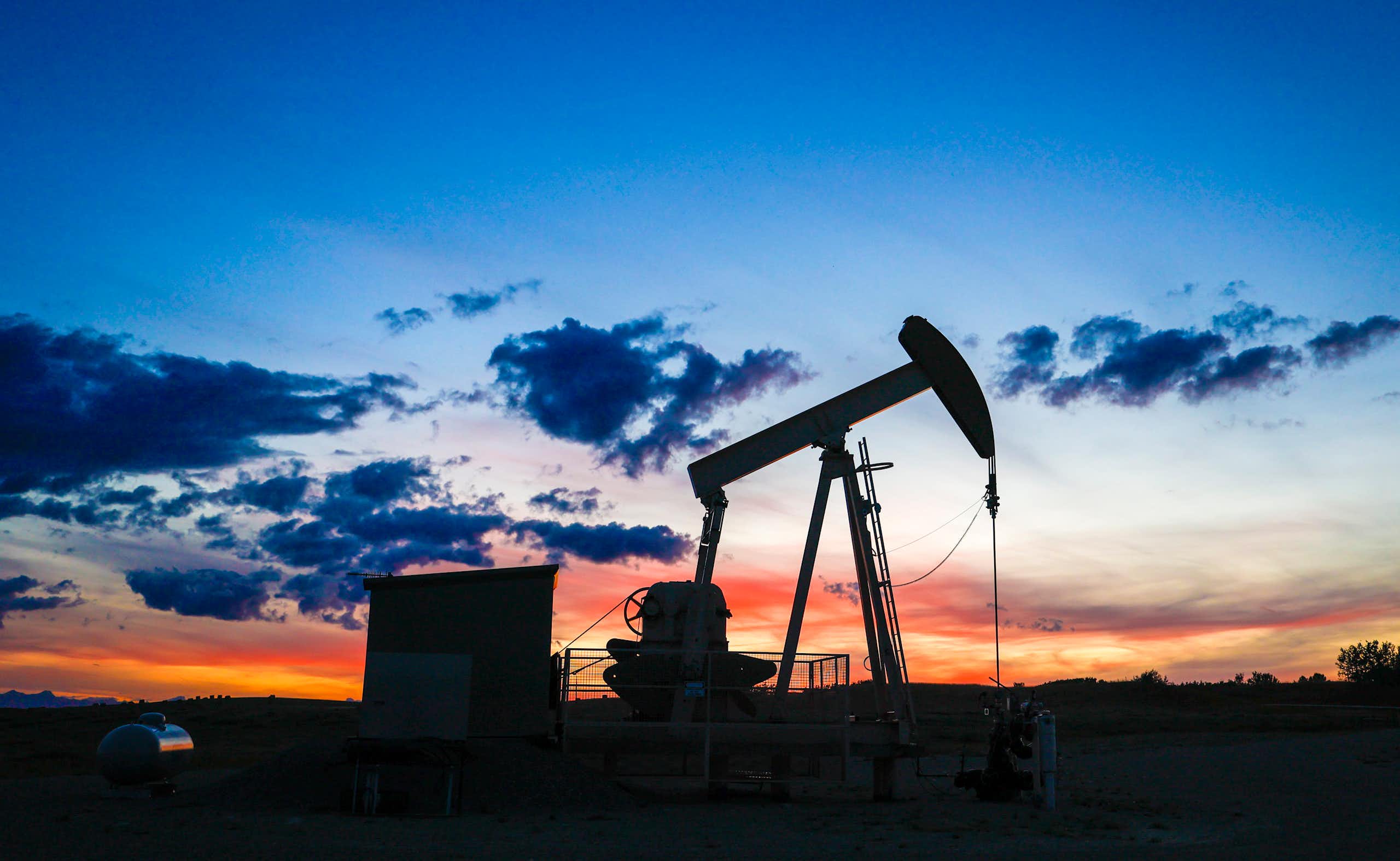Silhouette of a pumpjack draws out oil from a wellhead against a sunset sky