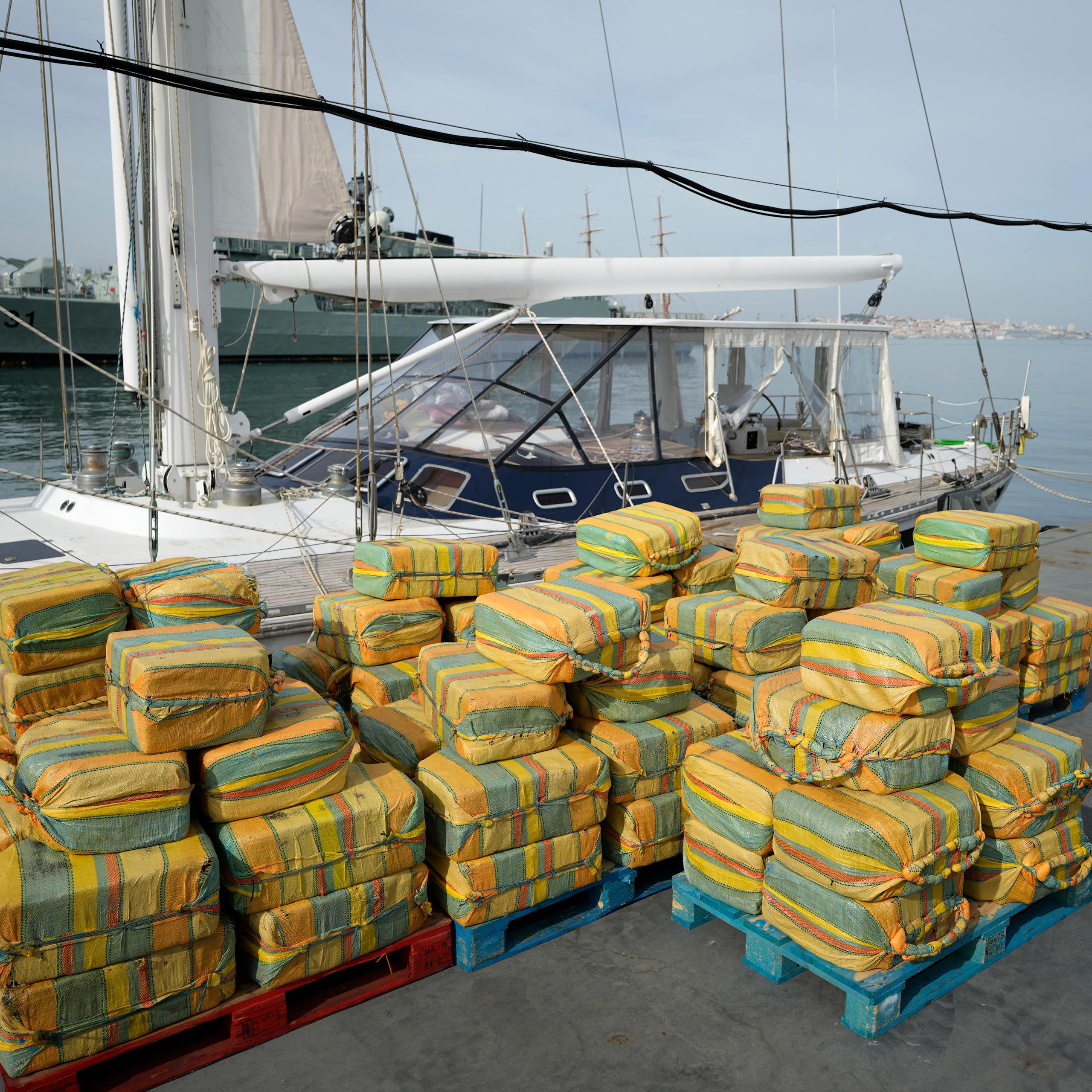 Decenas de fardos de cocaína apilados frente a un velero en el puerto.