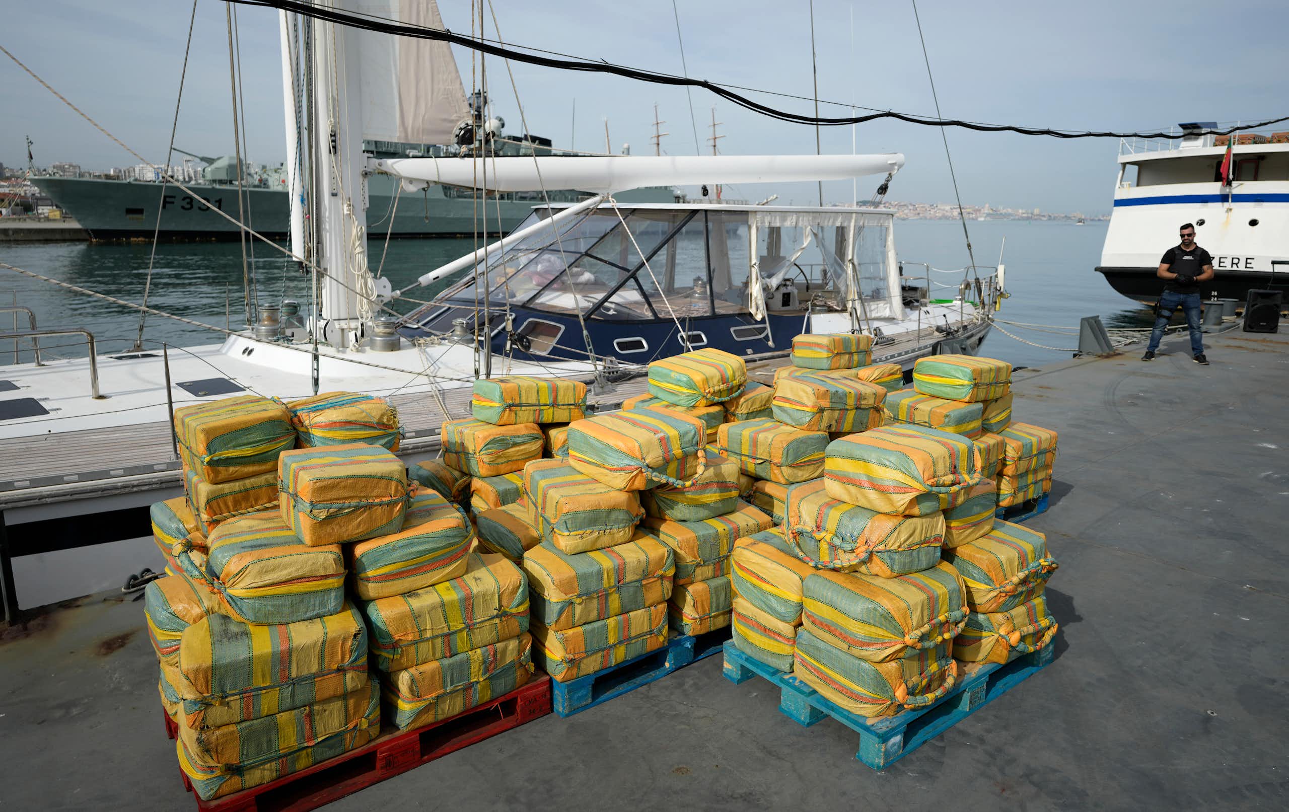 Decenas de fardos de cocaína apilados frente a un velero en el puerto.