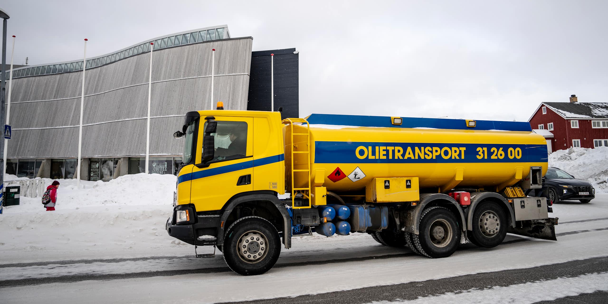 A yellow truck with an oil tank on the bank in a snowy street.