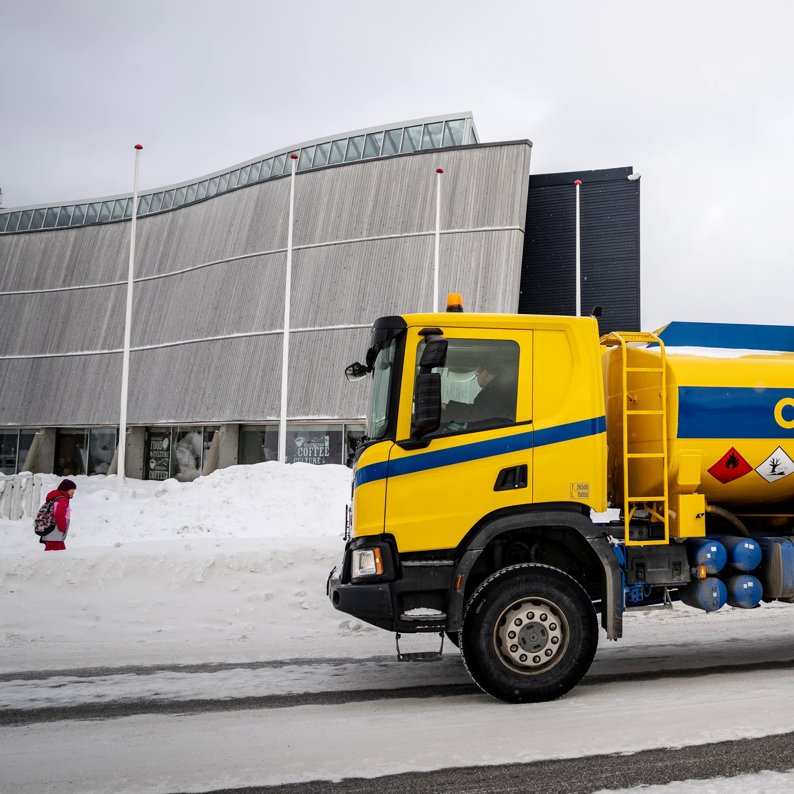 A yellow truck with an oil tank on the bank in a snowy street.