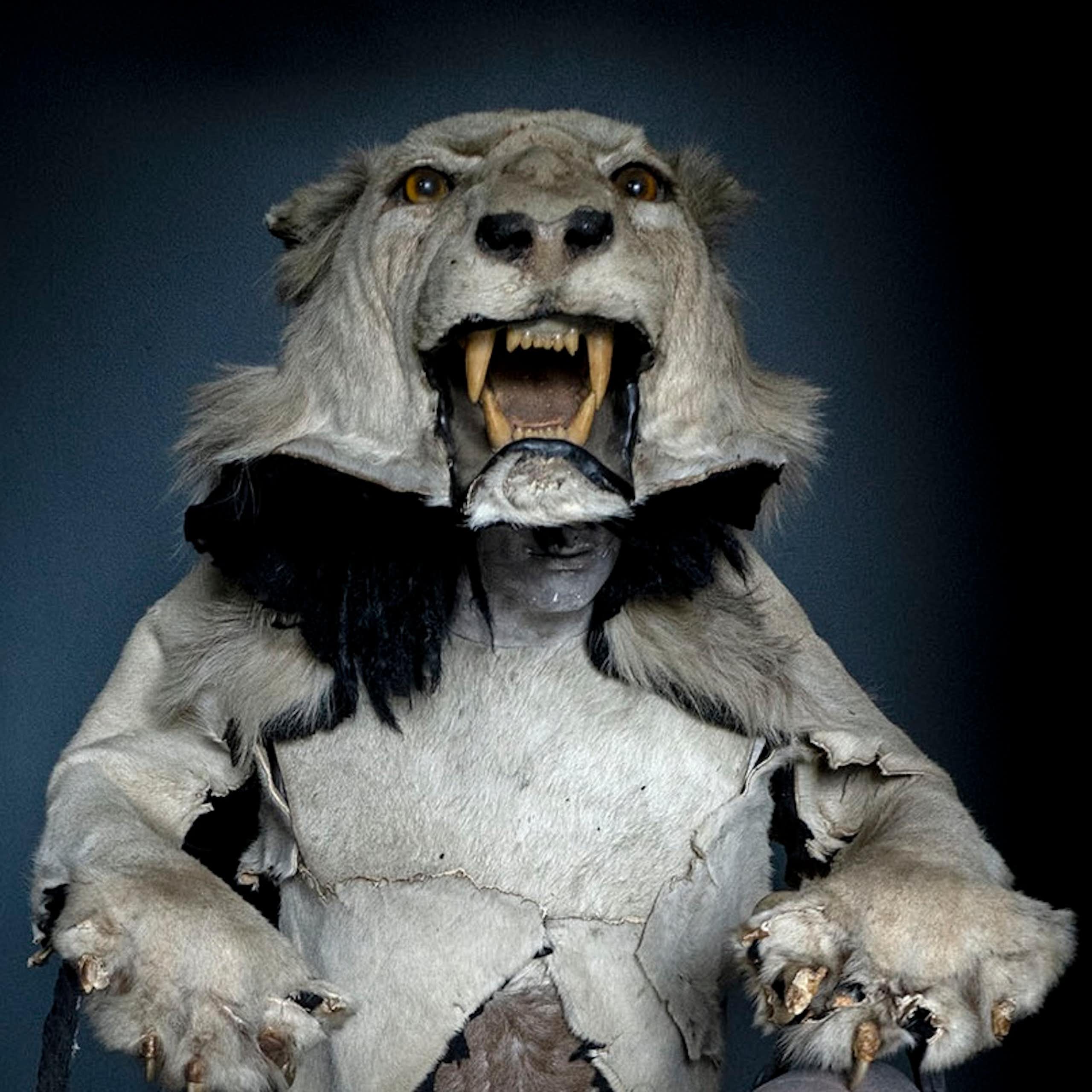 A mannequin wearing a stuffed lion's head as a hat. The lion holds two bags, each with a humanlike head in them.