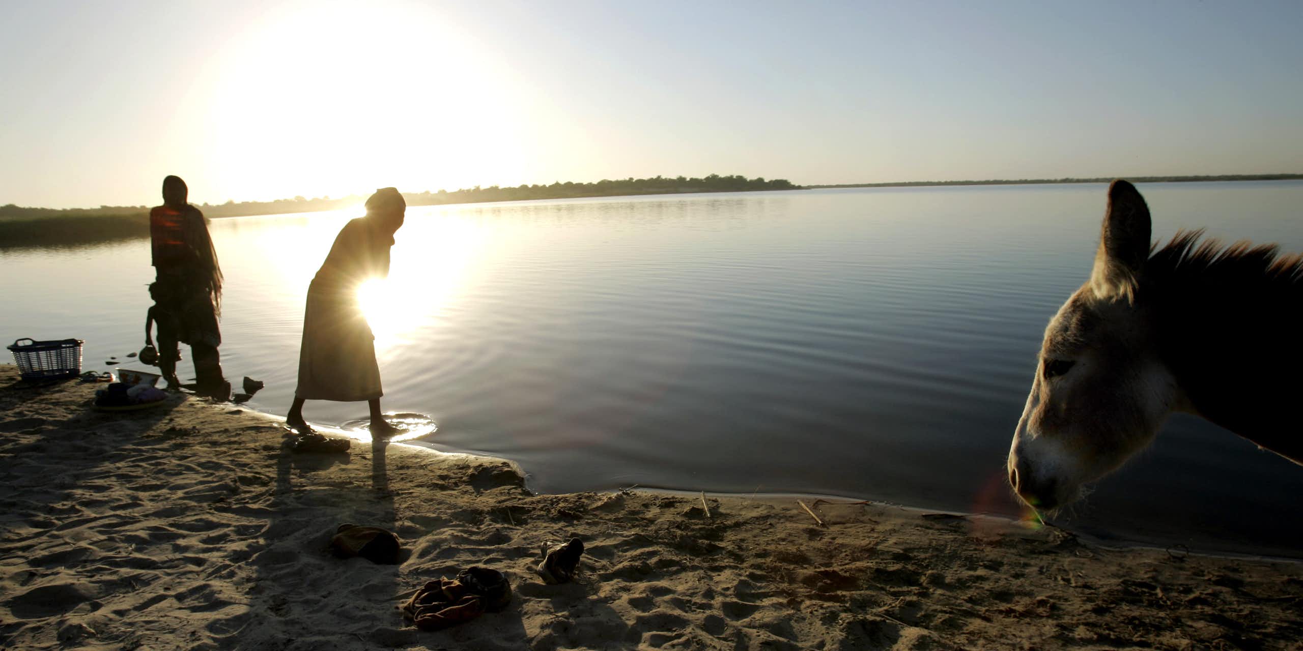 Pessoas lavam roupas na beira do Lago Chade com o pôr do sol sobre a água.