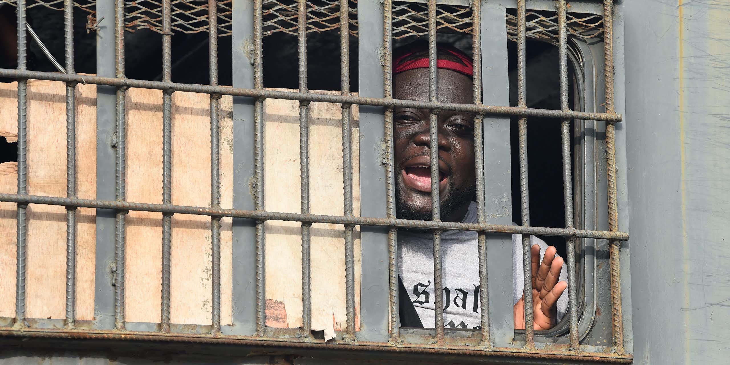 An African man speaks from behind bars in a police van.