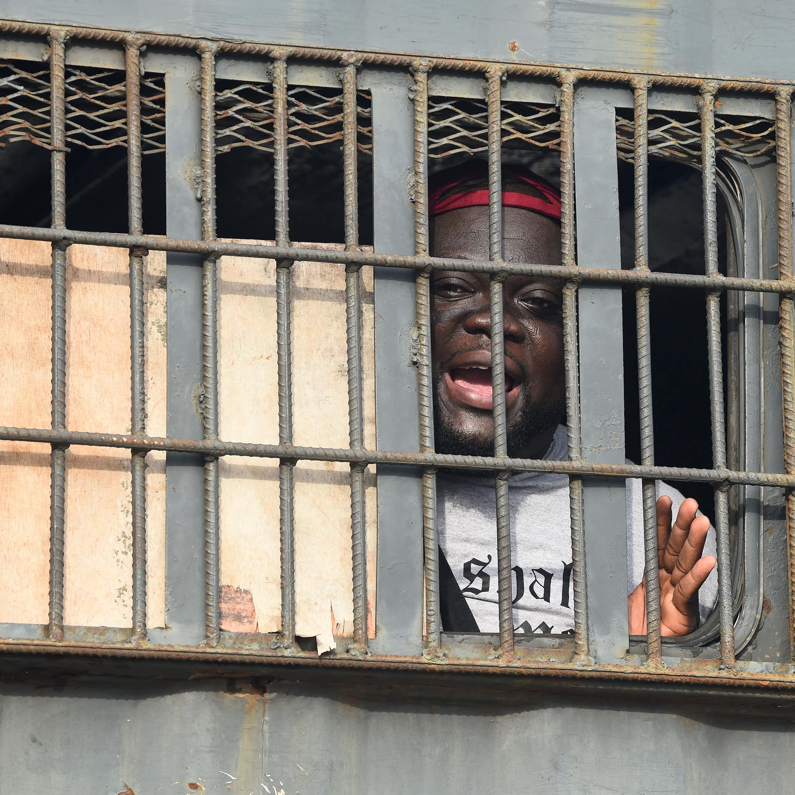 An African man speaks from behind bars in a police van.