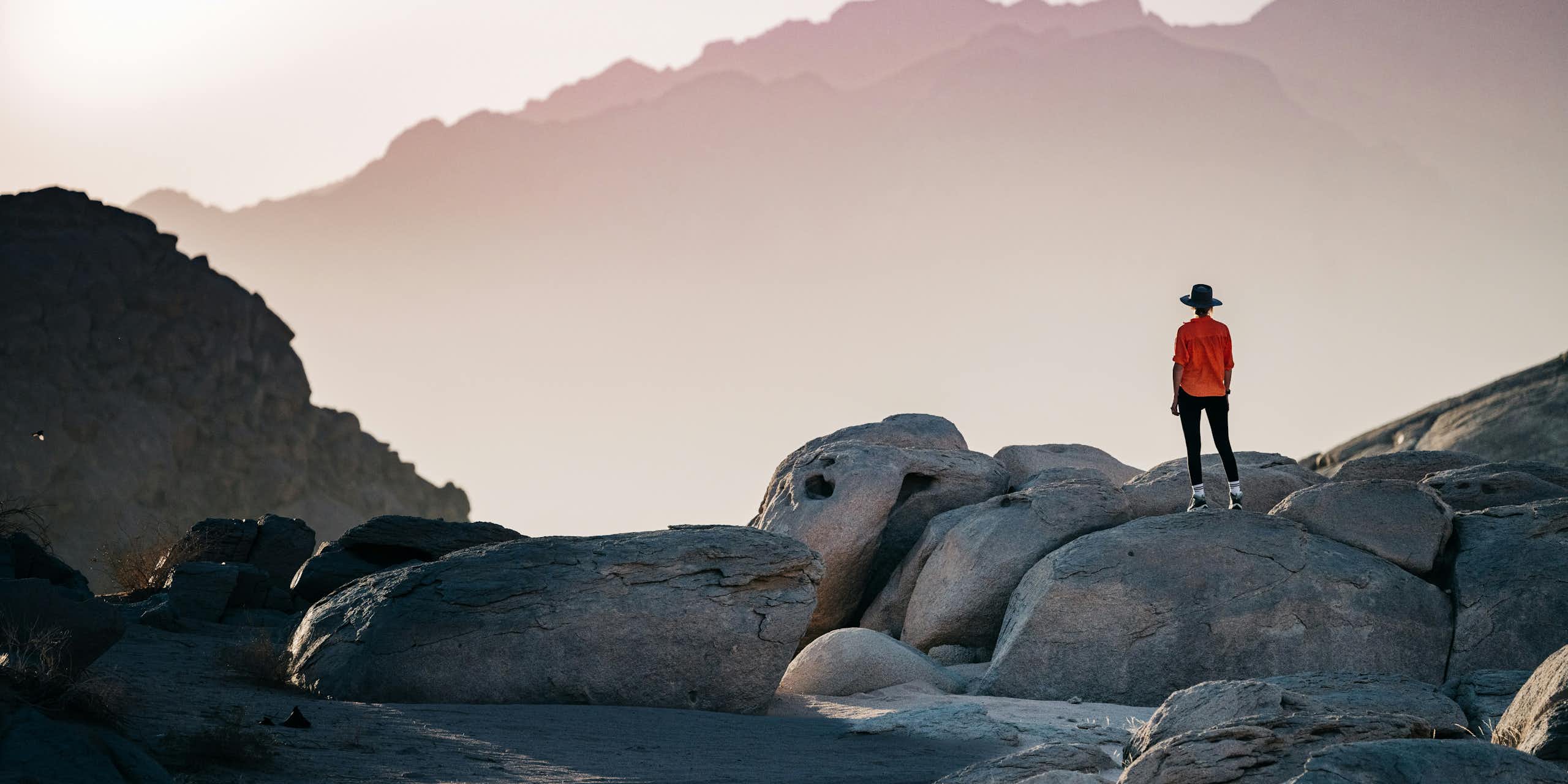 A person standing on a rock formation looking toward a mountain