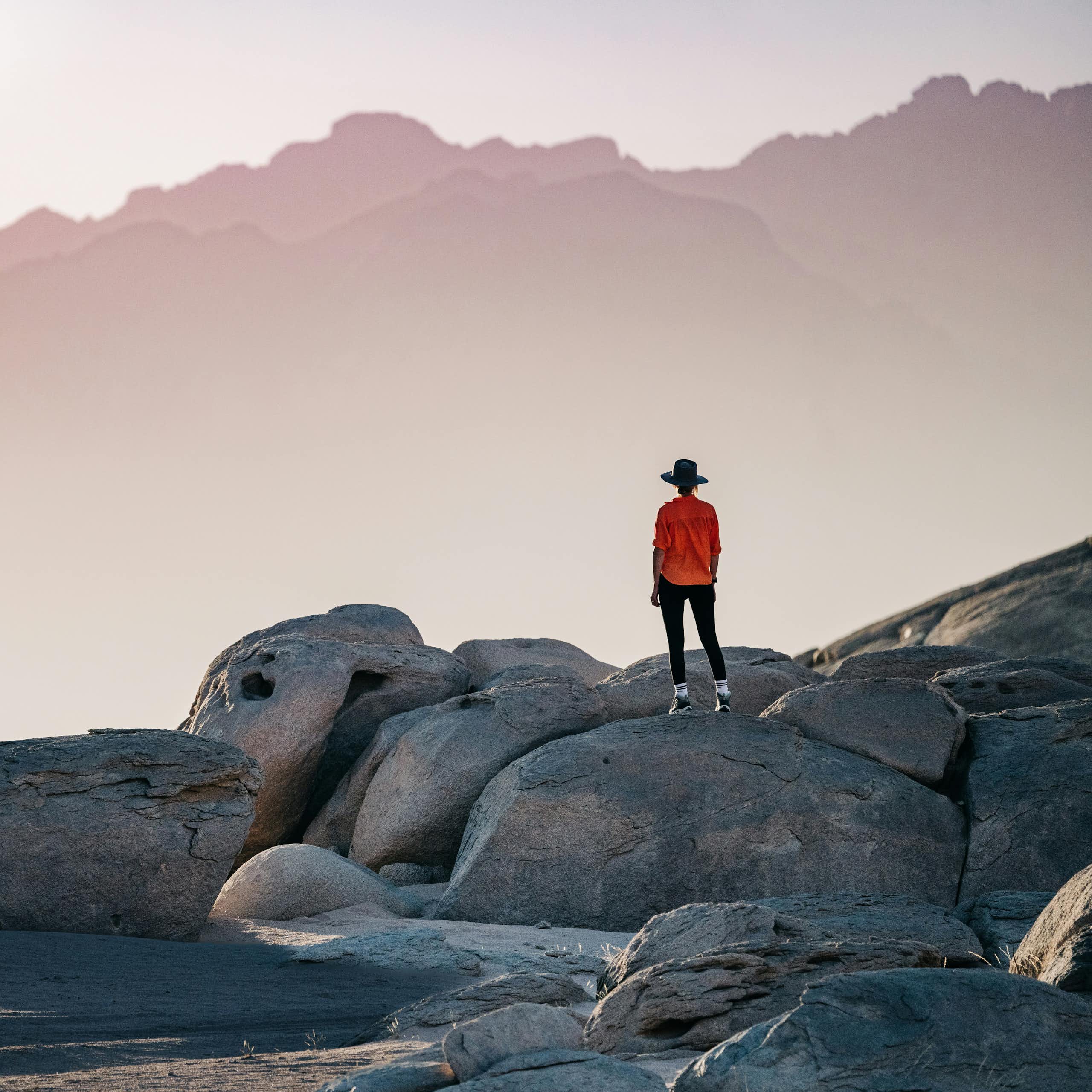 A person standing on a rock formation looking toward a mountain