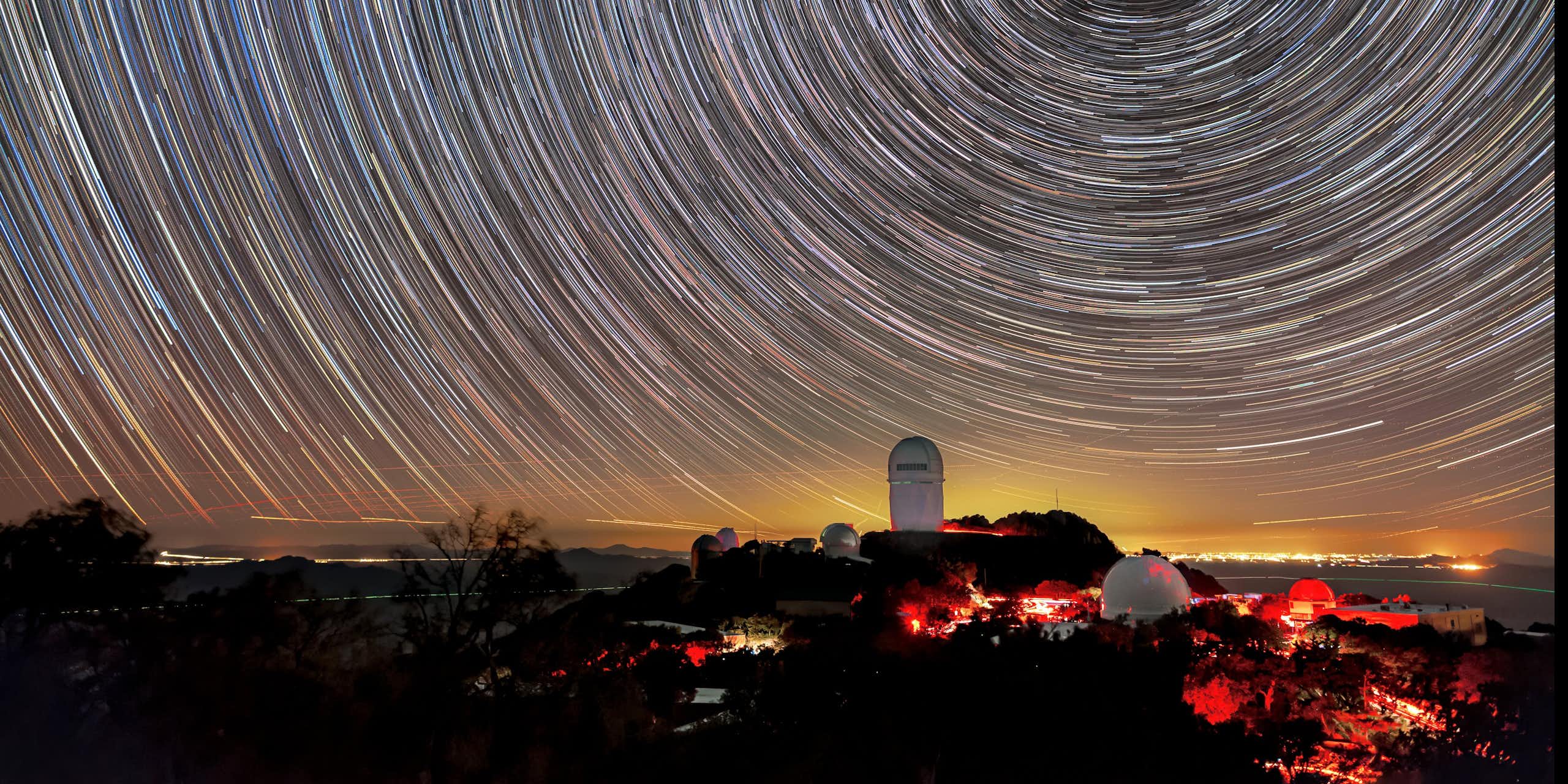 Timelapse photo showing star trails in the night sky above a large telescope building.
